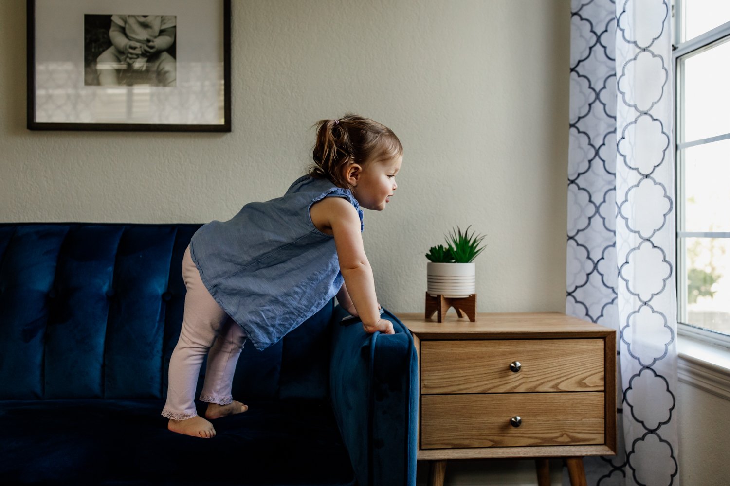 toddler standing on blue couch facing window