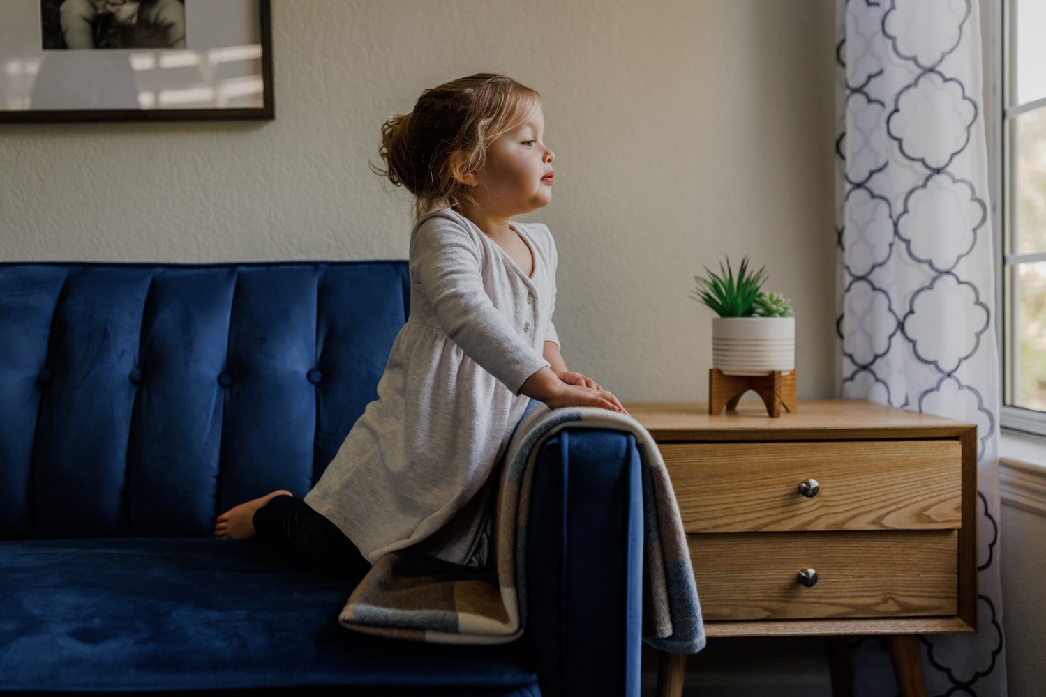 little girl kneeling on blue couch and looking for something outside