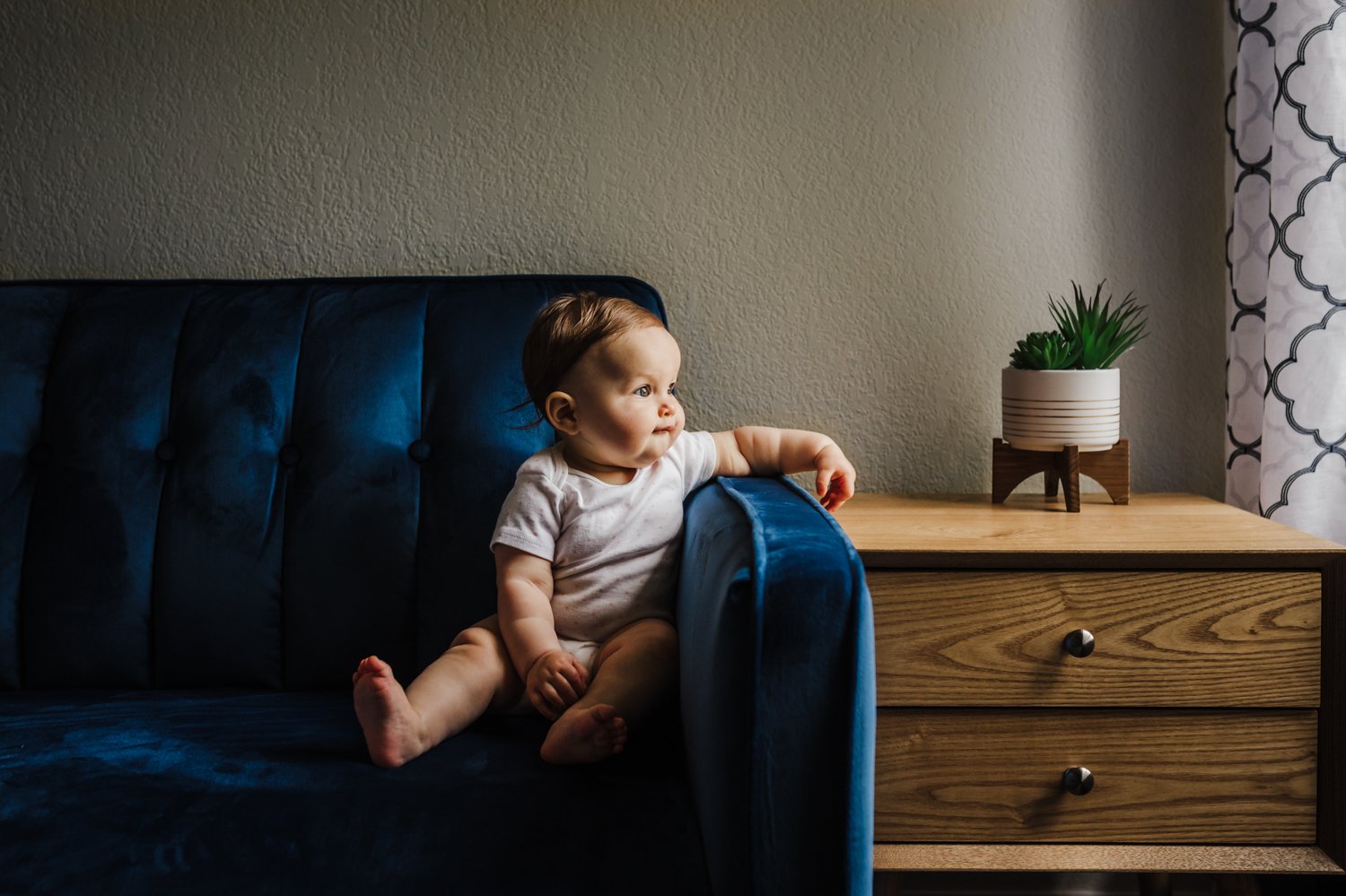 baby sitting on blue couch looking out window