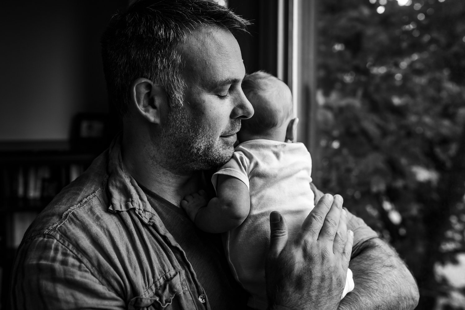 dad holding newborn close to face snuggling him and patting his back