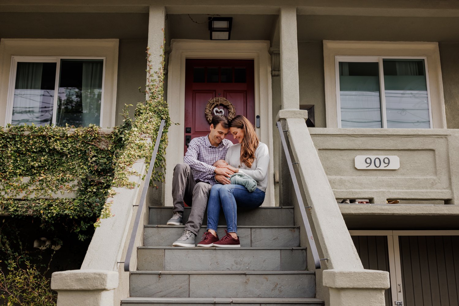 parents sitting on front porch holding and looking down and smiling at newborn in their laps