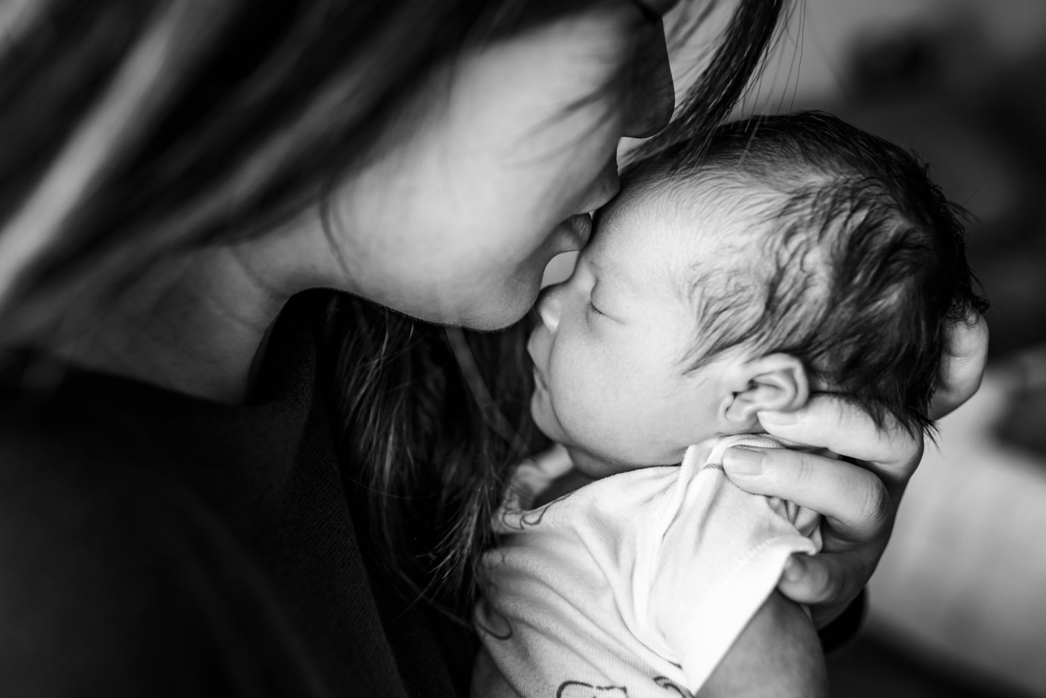 mom holding newborn close and kissing baby's forehead