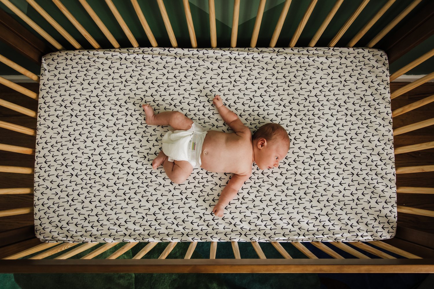 birds-eye view of newborn laying in crib in diaper