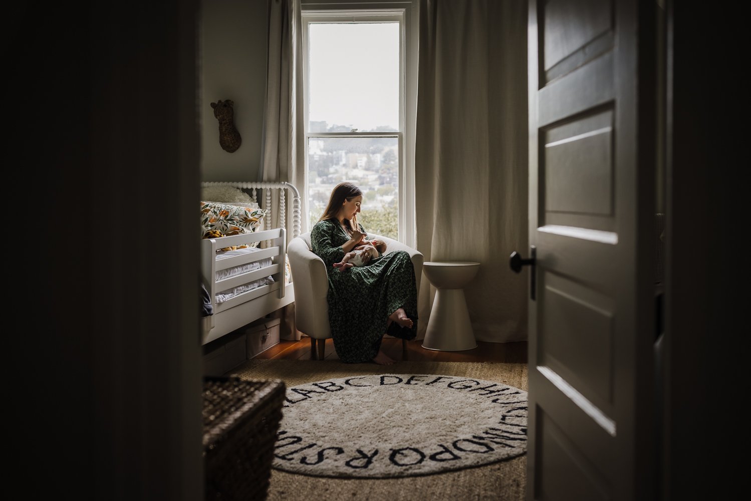 mom in green dress sitting in front of window nursing her baby