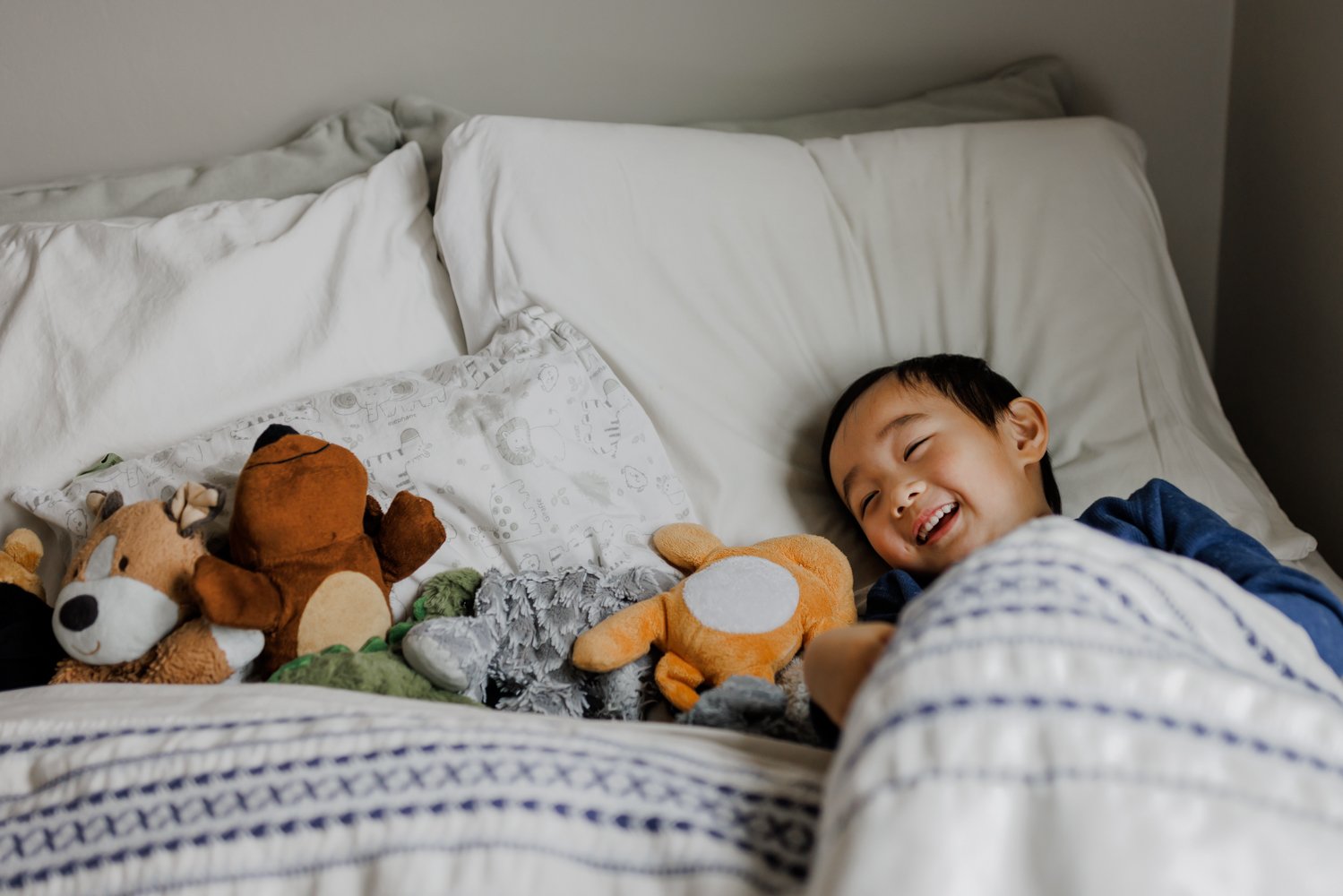 4-year-old boy laying in his bed next to all of his favorite stuffed animals