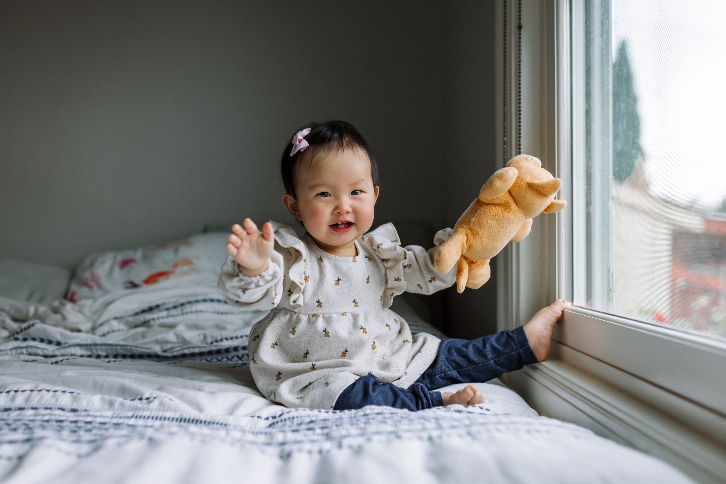 baby-girl-sitting-on-bed-with-stuffed-animals-laughing.jpg