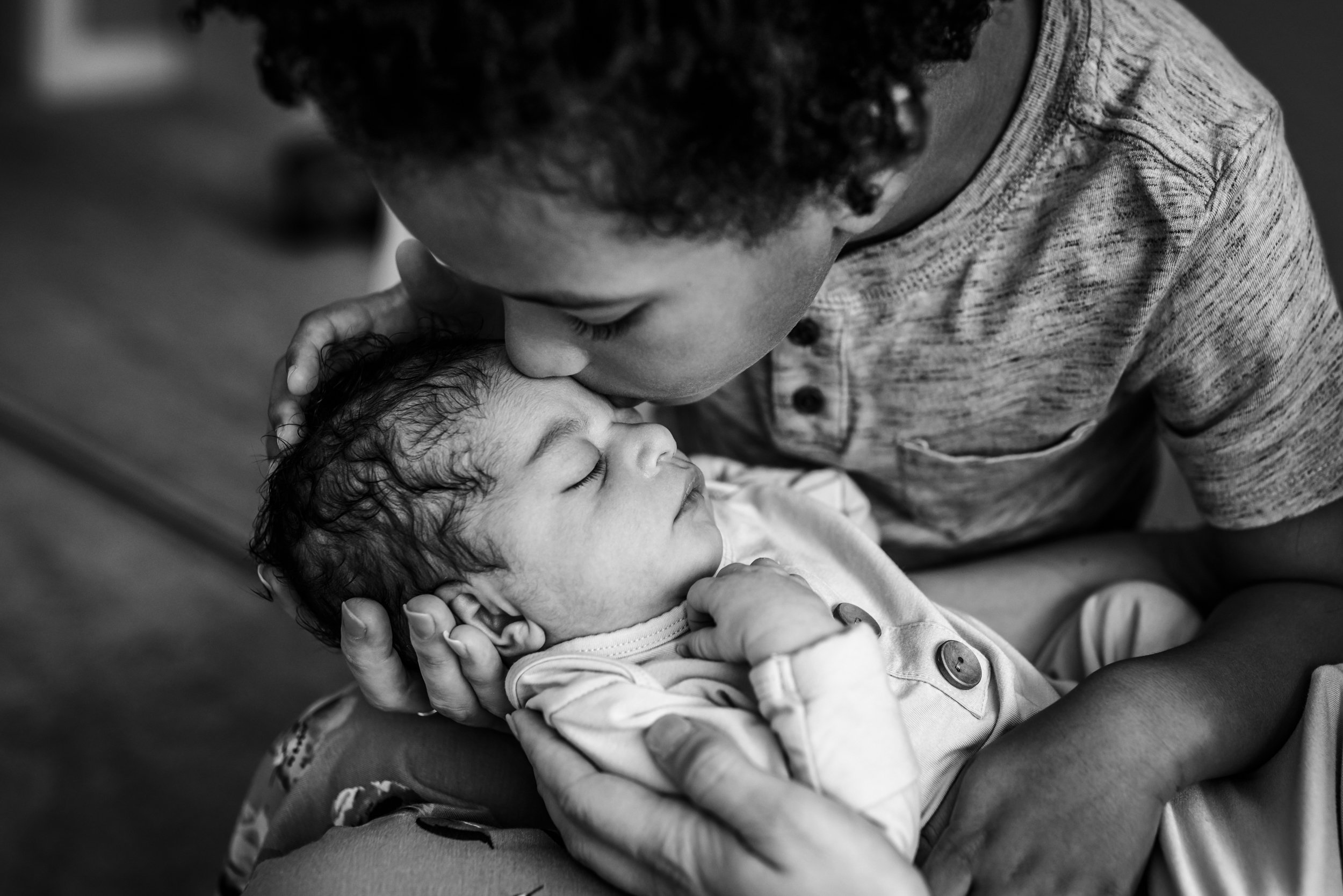 black and white close up of a 4-year-old boy kissing his newborn sister