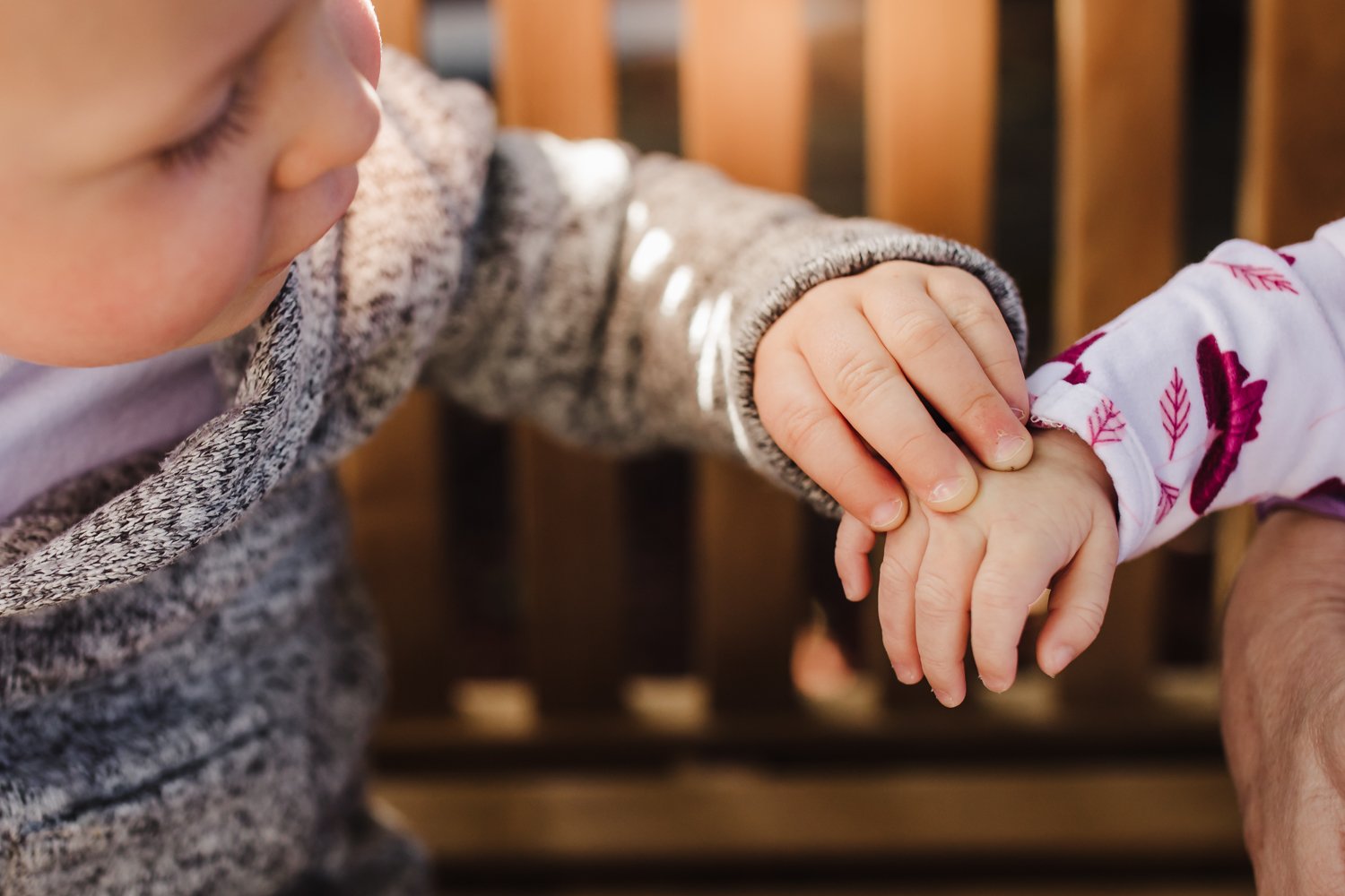  close up of toddler boy reaching for and touching the top of his baby sister's hand