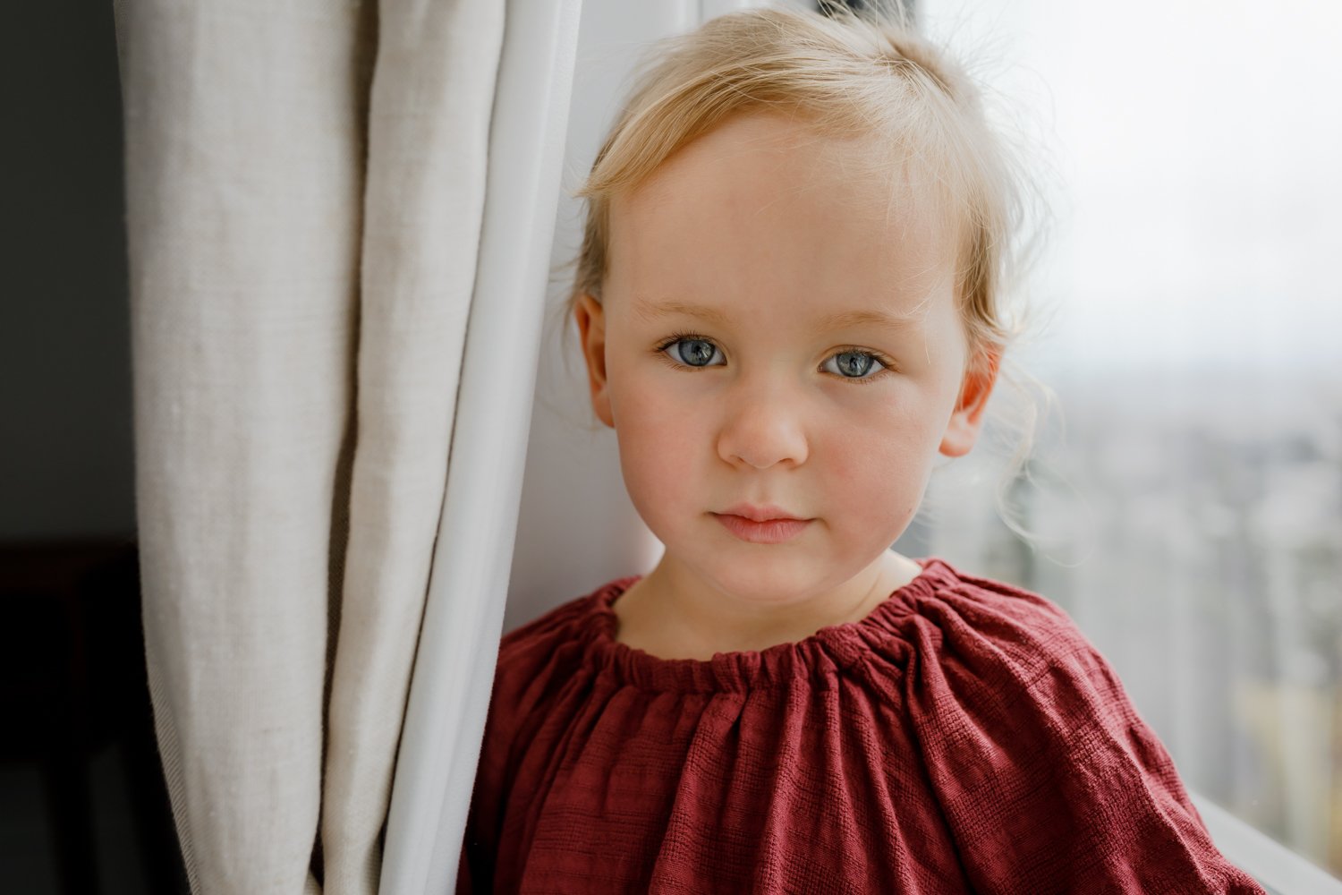 portrait of a 4-year-old girl standing next to a curtain and looking at the camera