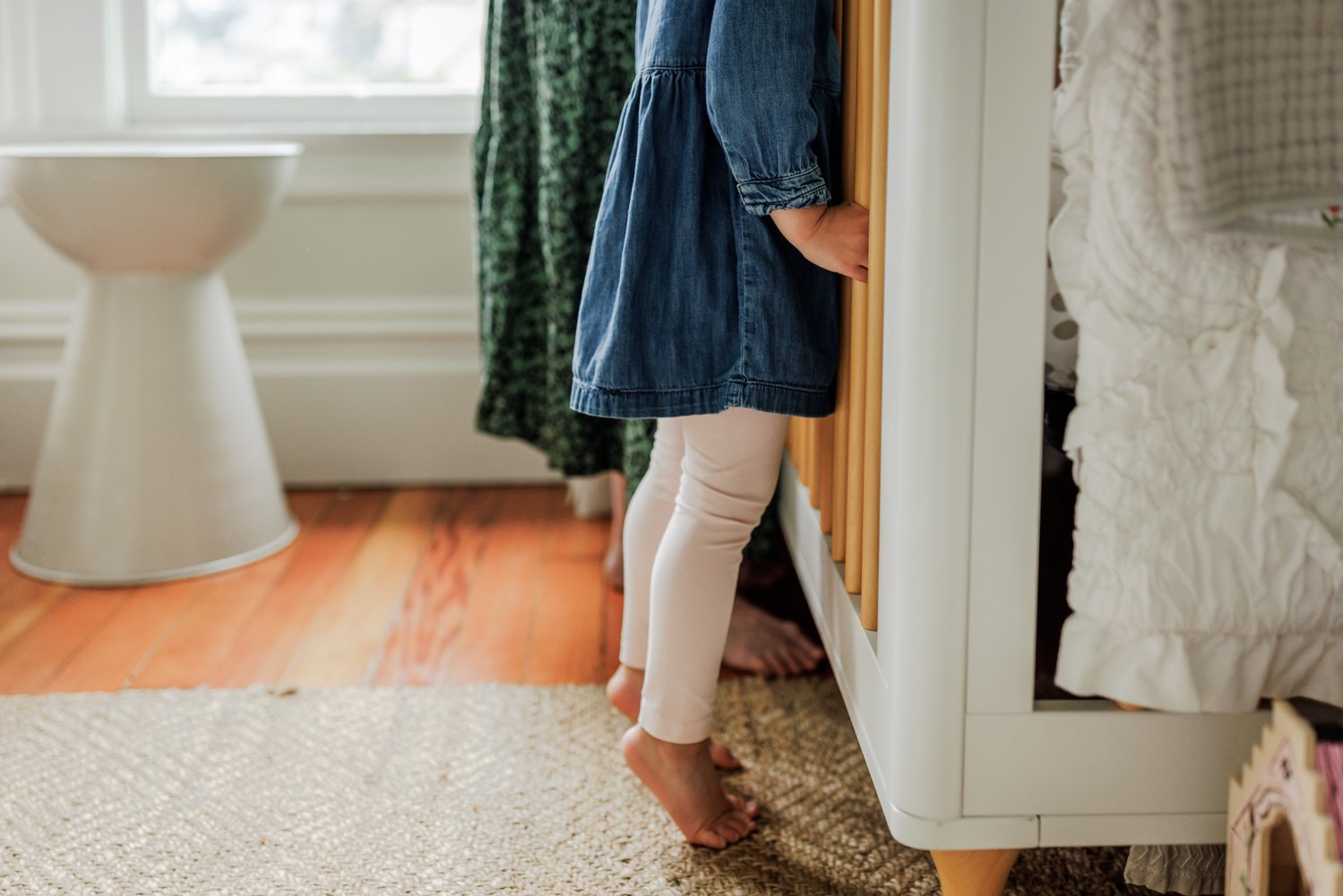 sister standing on the tips of her toes to peer into the top of her newborn sibling's crib