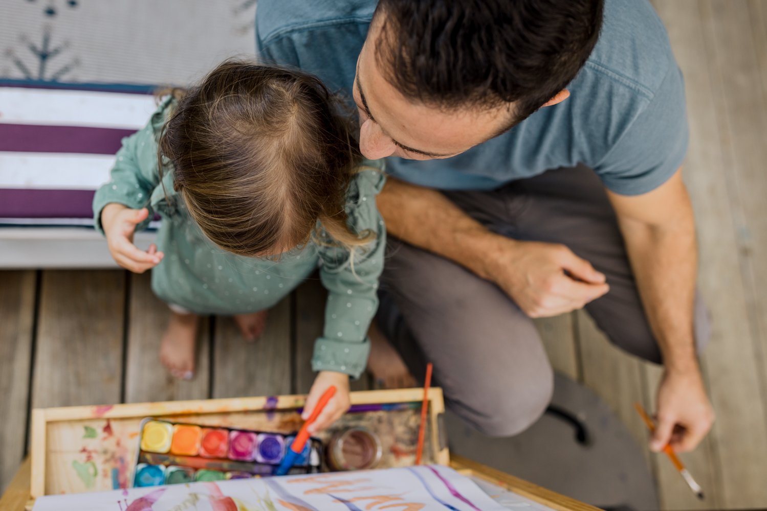 birdseye view of a dad and toddler girl sitting at an easel and painting together