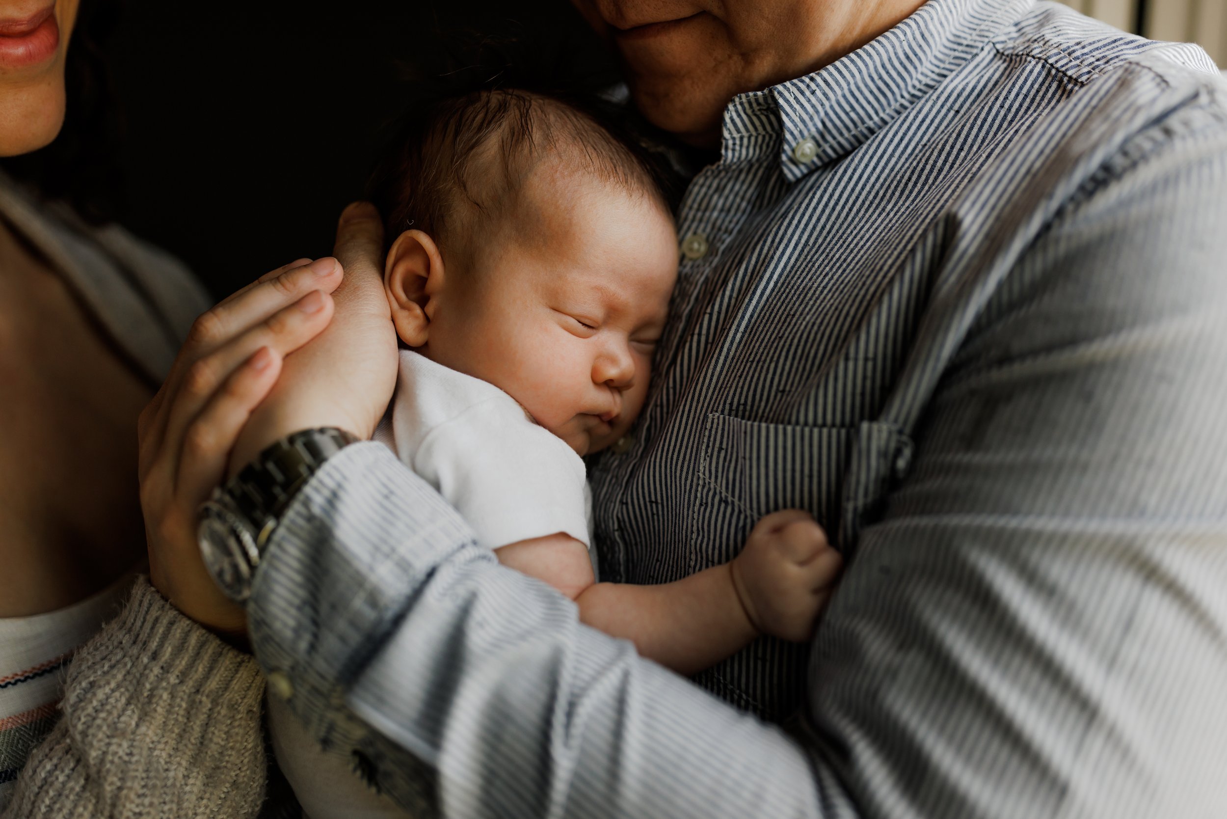 newborn sleeping on dad's chest while mom and dad rest their hands on the back of the baby