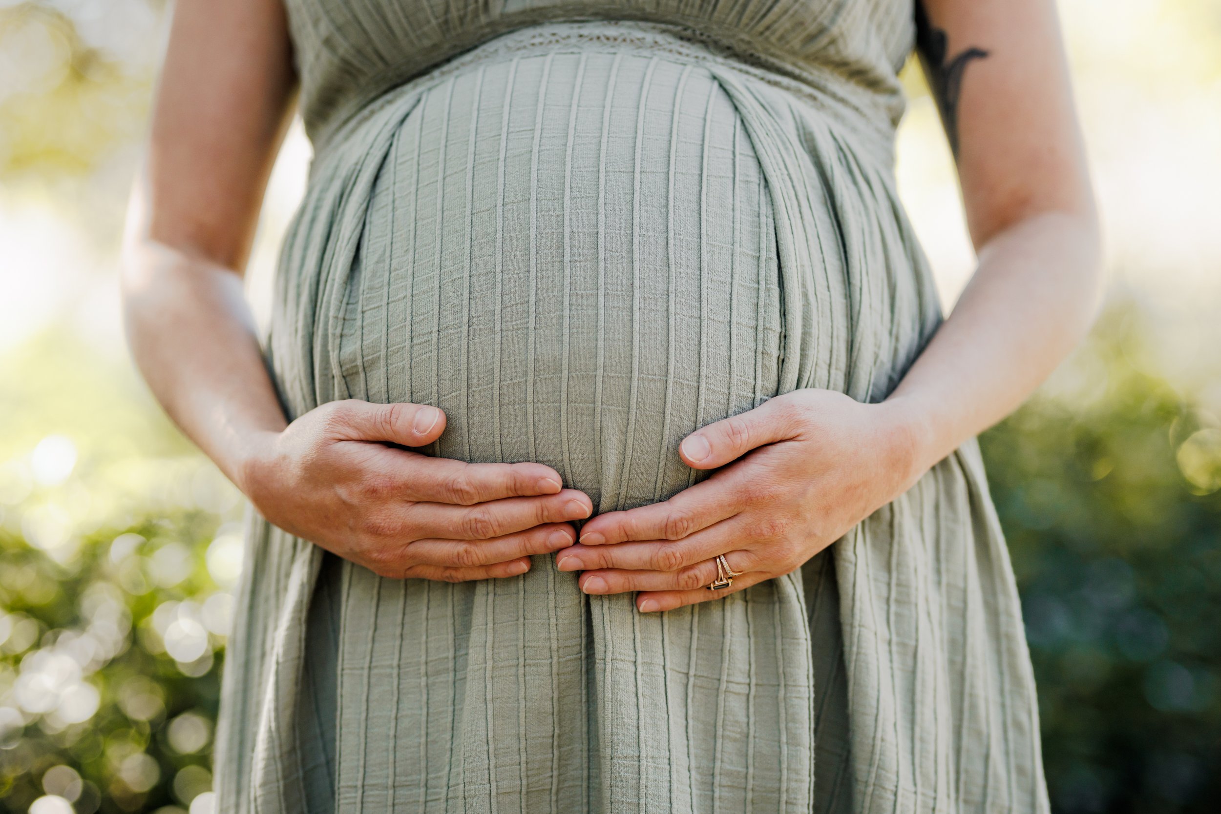 mom resting her hand on her baby bump standing in front of greenery