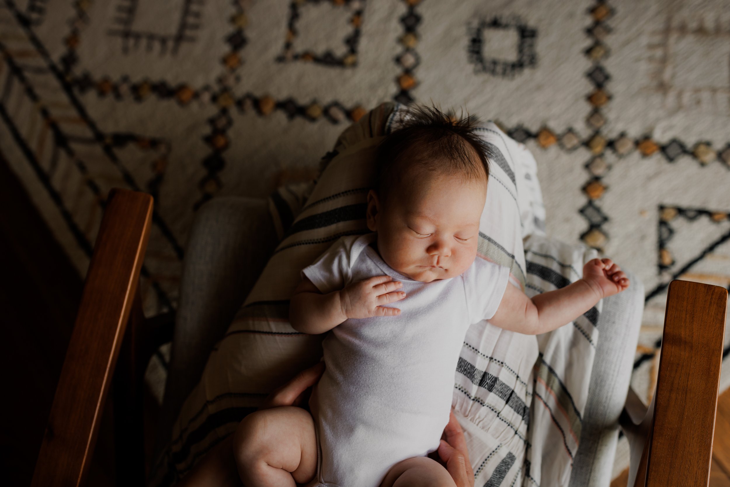 birds eye view of baby sleeping in mom's lap as she sits in chair and baby's arm is hanging down