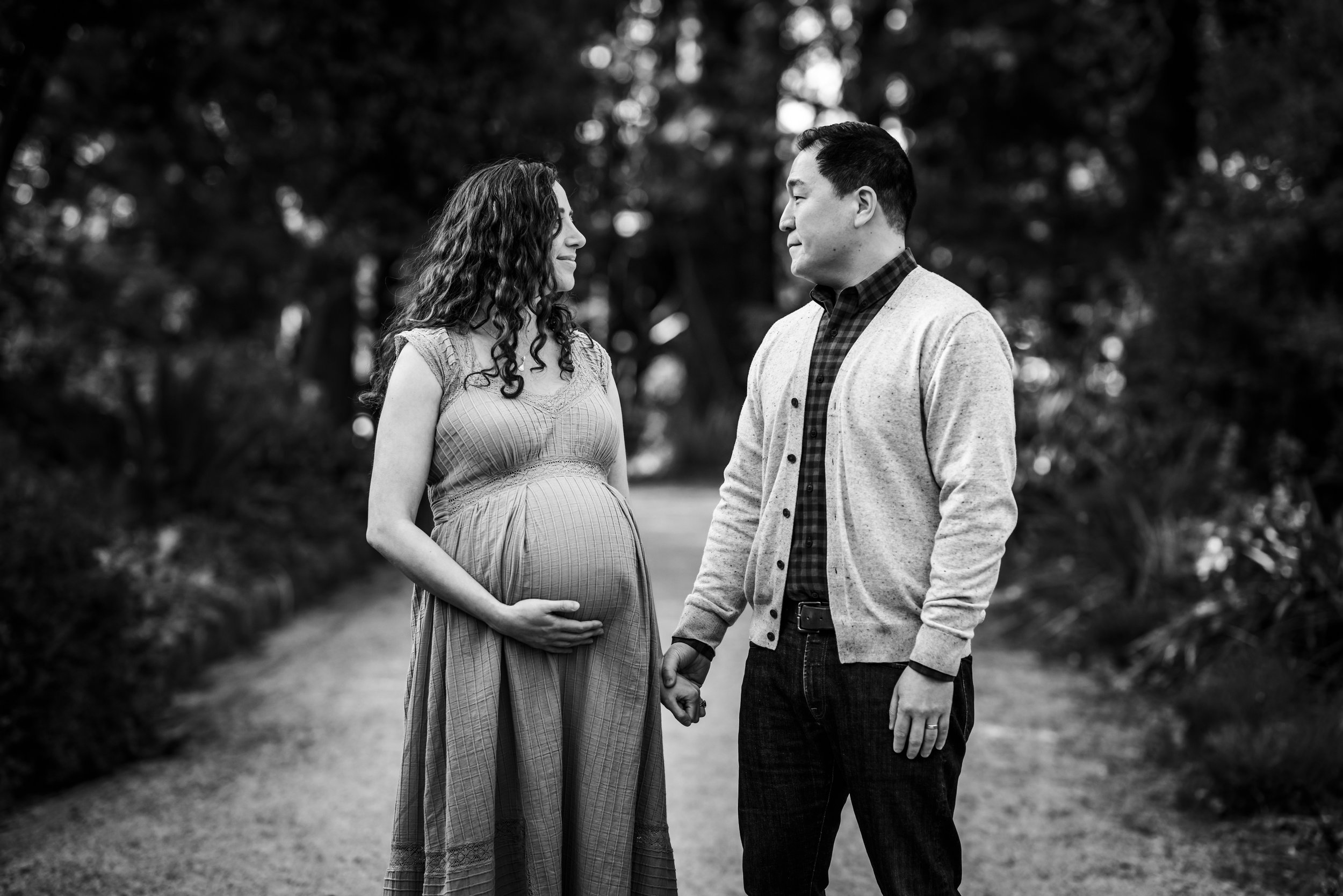 expecting mom and husband looking at each other and holding hands at Berkeley Gardens as mom touches baby bump