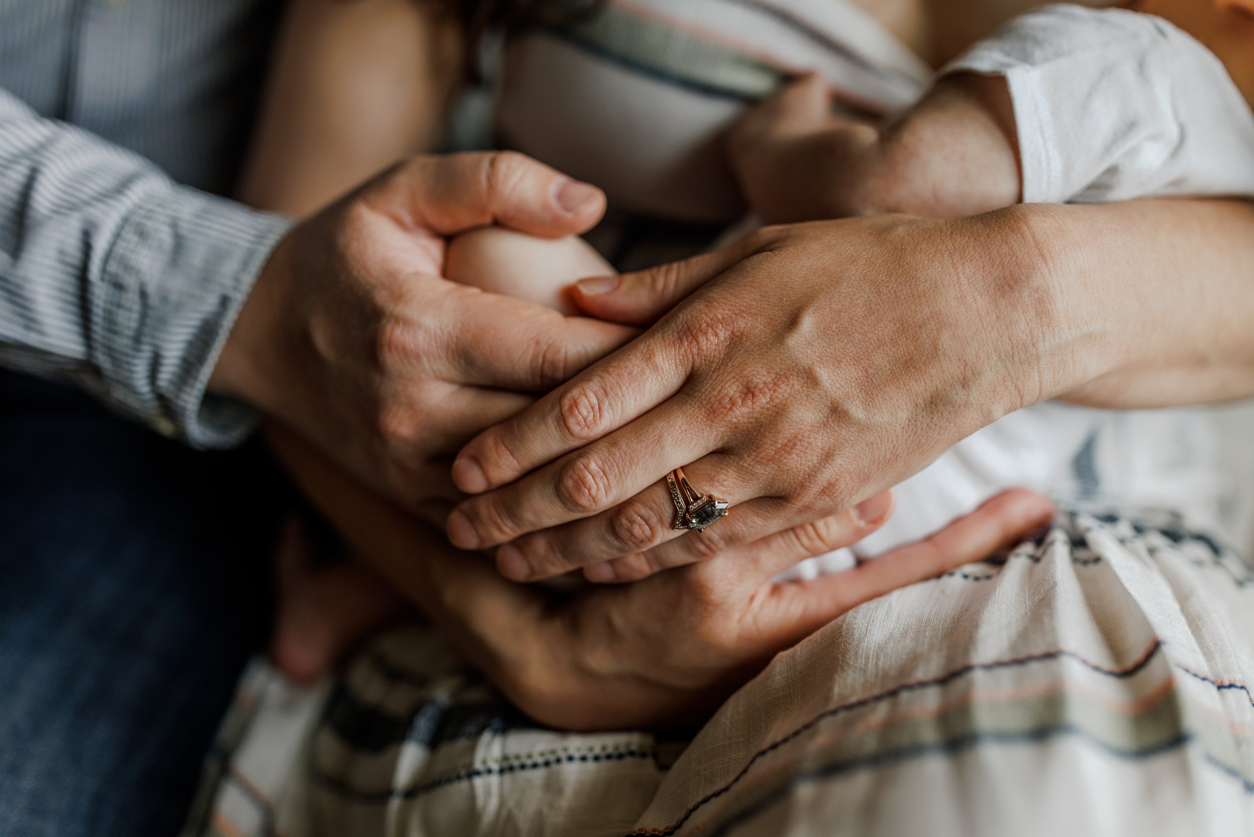 close up of parents' hands overlapping while holding newborn