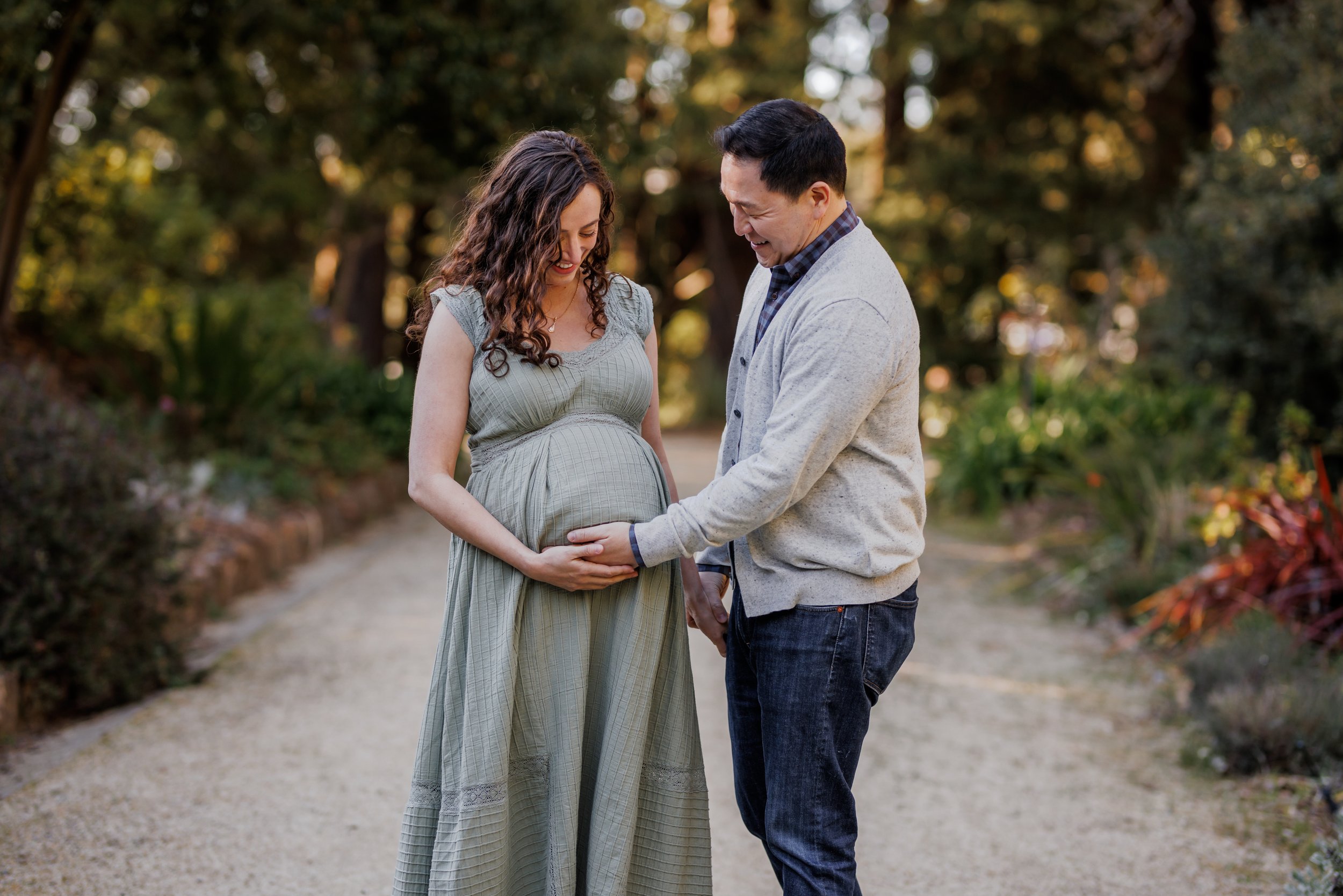 expecting couple standing close on a path in Blake Gardens holding hands on baby bump