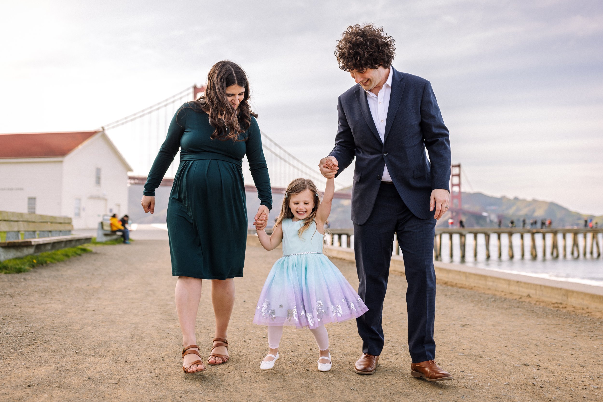 parents walking with their daughter holding her hand and laughing with the golden gate bridge in the background