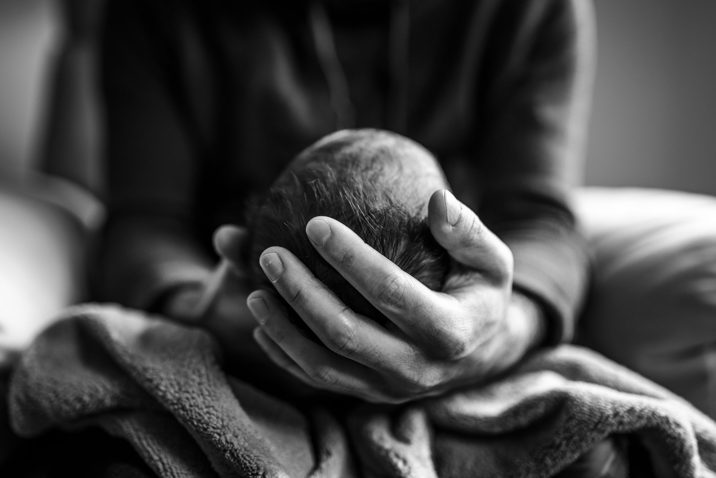 black and white close up of Dad's hand holding newborn baby's head