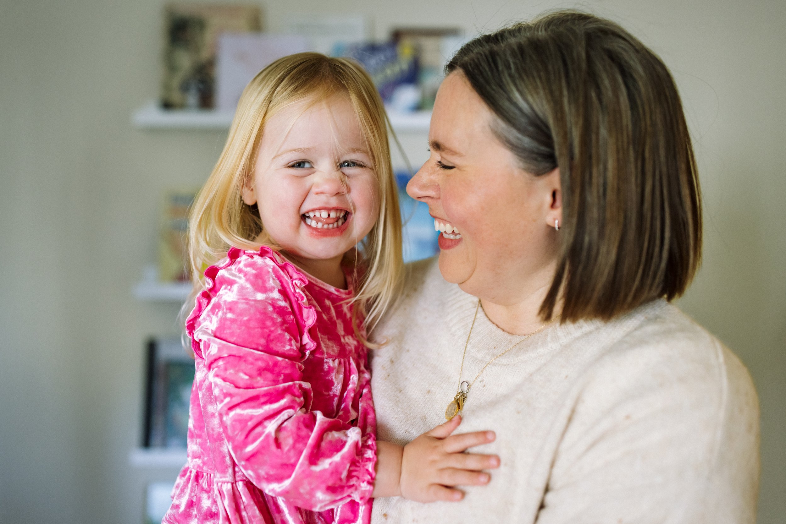 daughter looking towards camera while mom holding her and mom looking at her and laughing