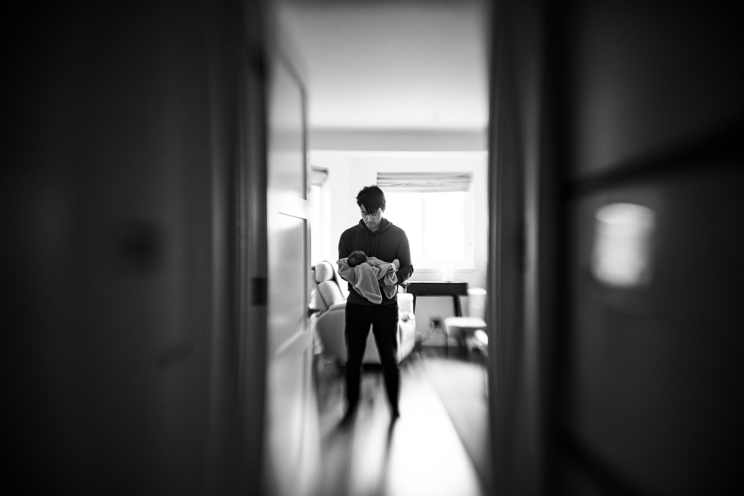 photo taken in doorway of dad comforting newborn baby in bedroom