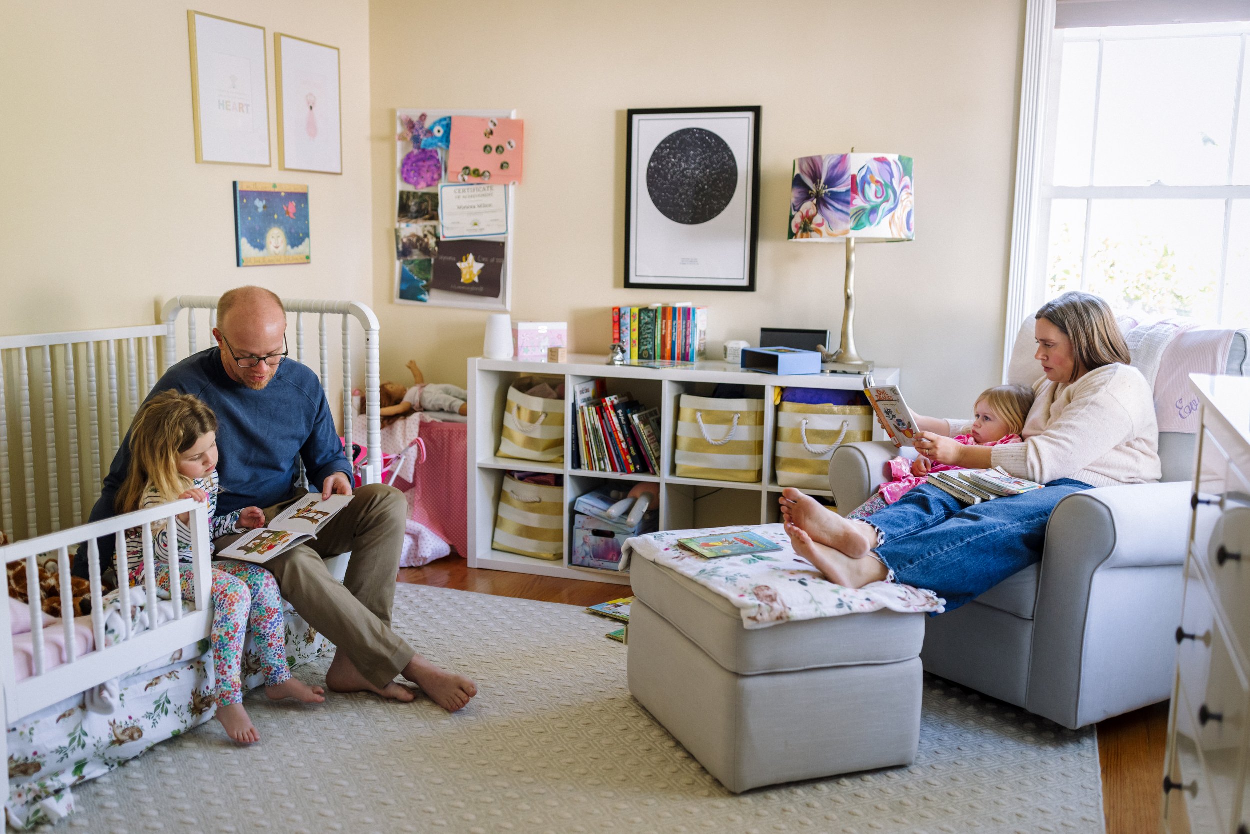 parents and two young daughters sitting in child's room reading separately to each of their girls