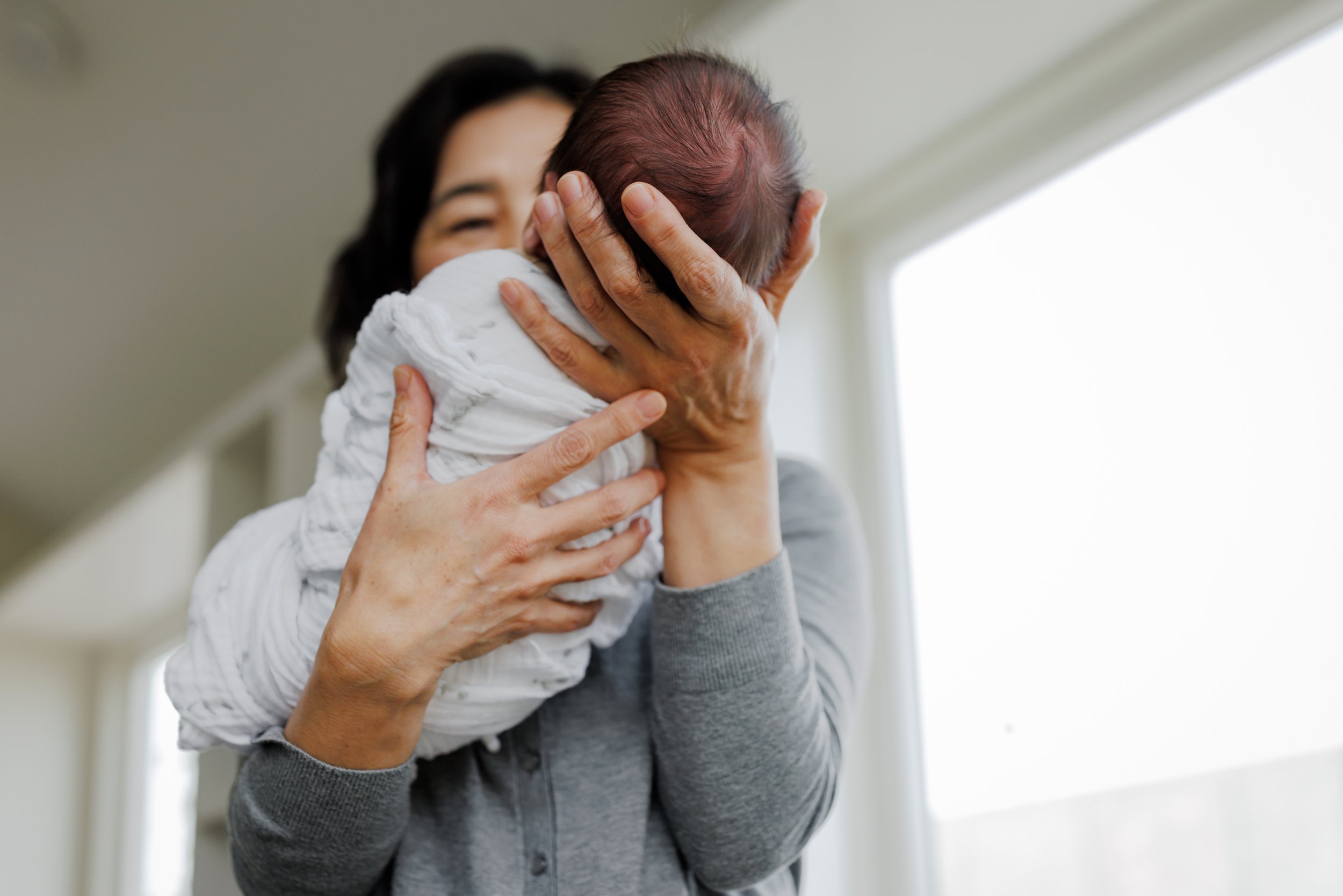 shot below of grandma holding newborn in her hands and bringing baby closer to her face