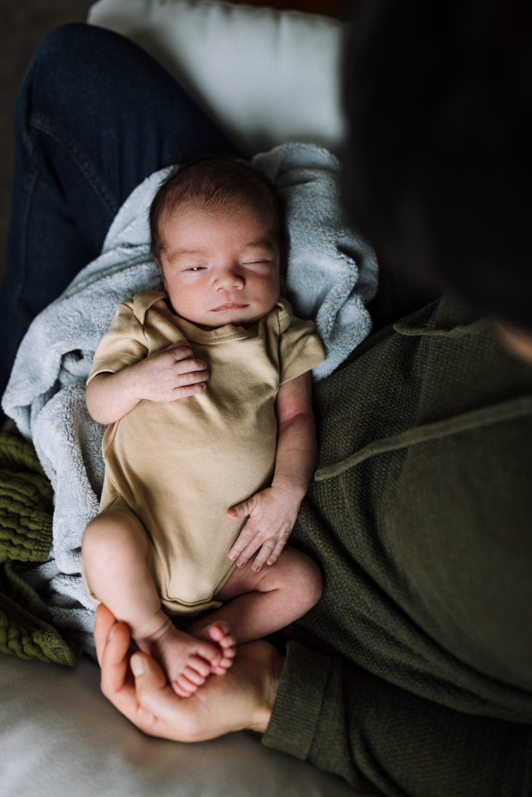 birds eye view of baby resting in dad's lap while surrounded by blankets with one eye open