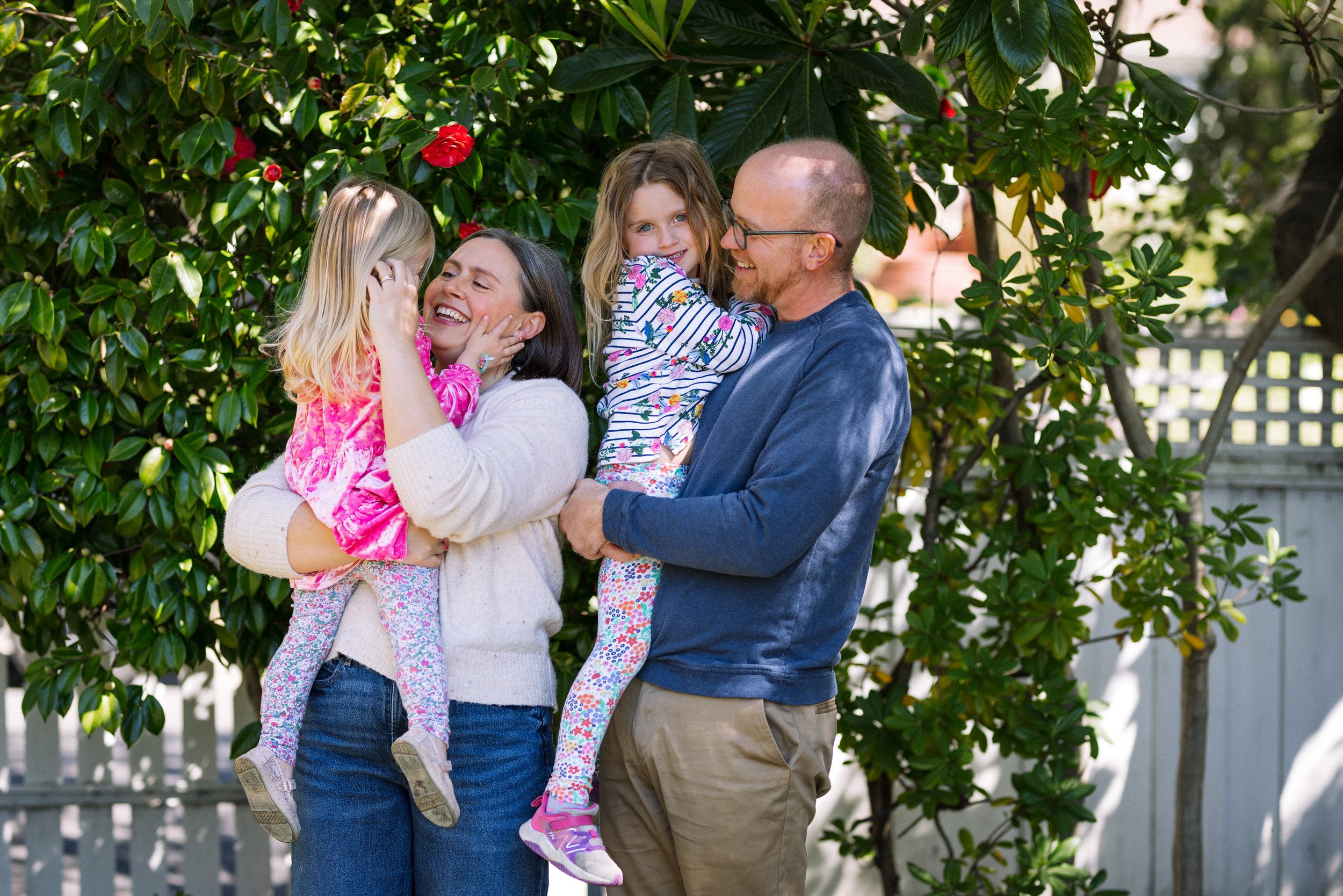 family together with mom and dad holding and looking at two young daughters and the older daughter is looking at the camera during a family photo session