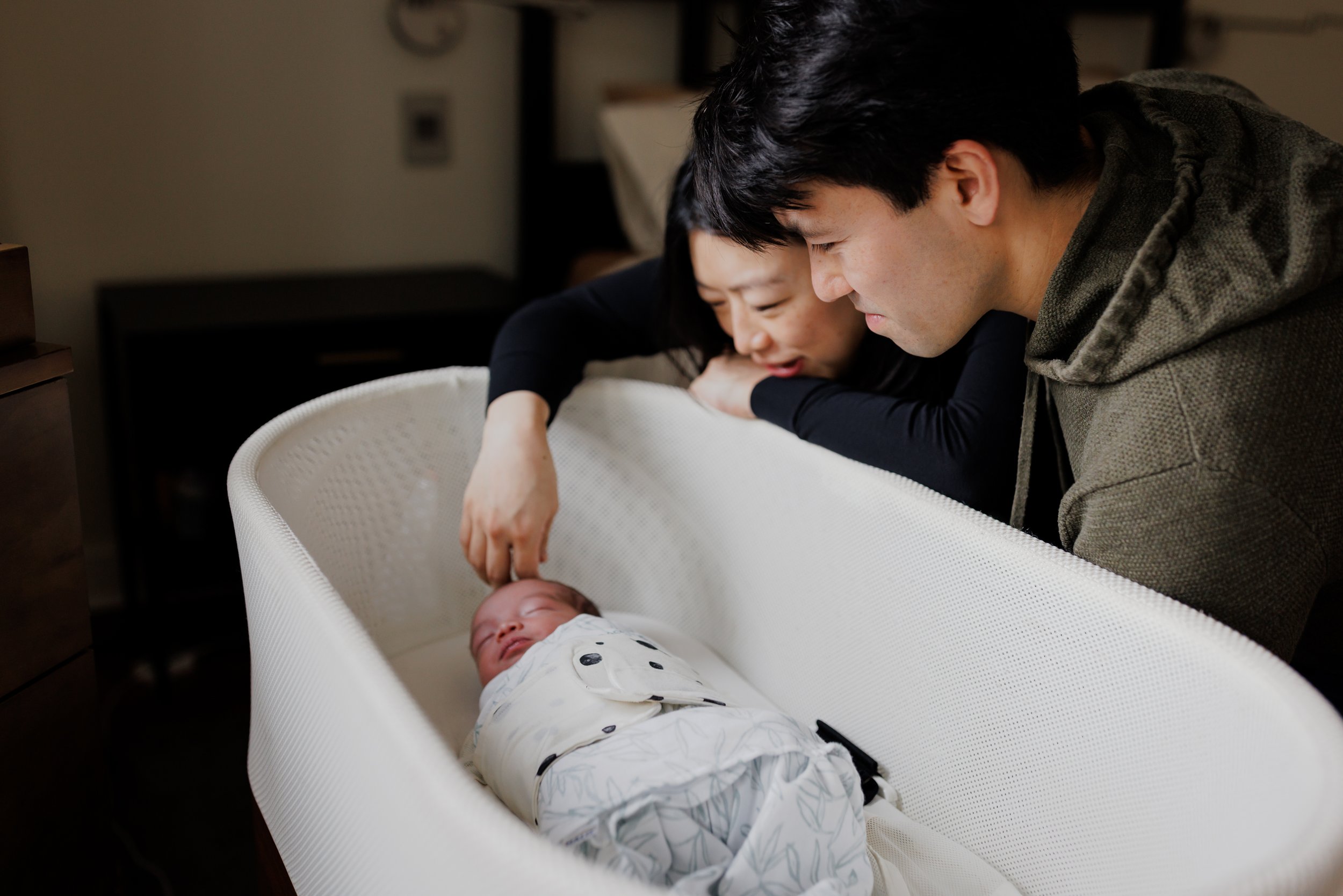 mom and dad leaning over and smiling at their baby sleeping in bassinet