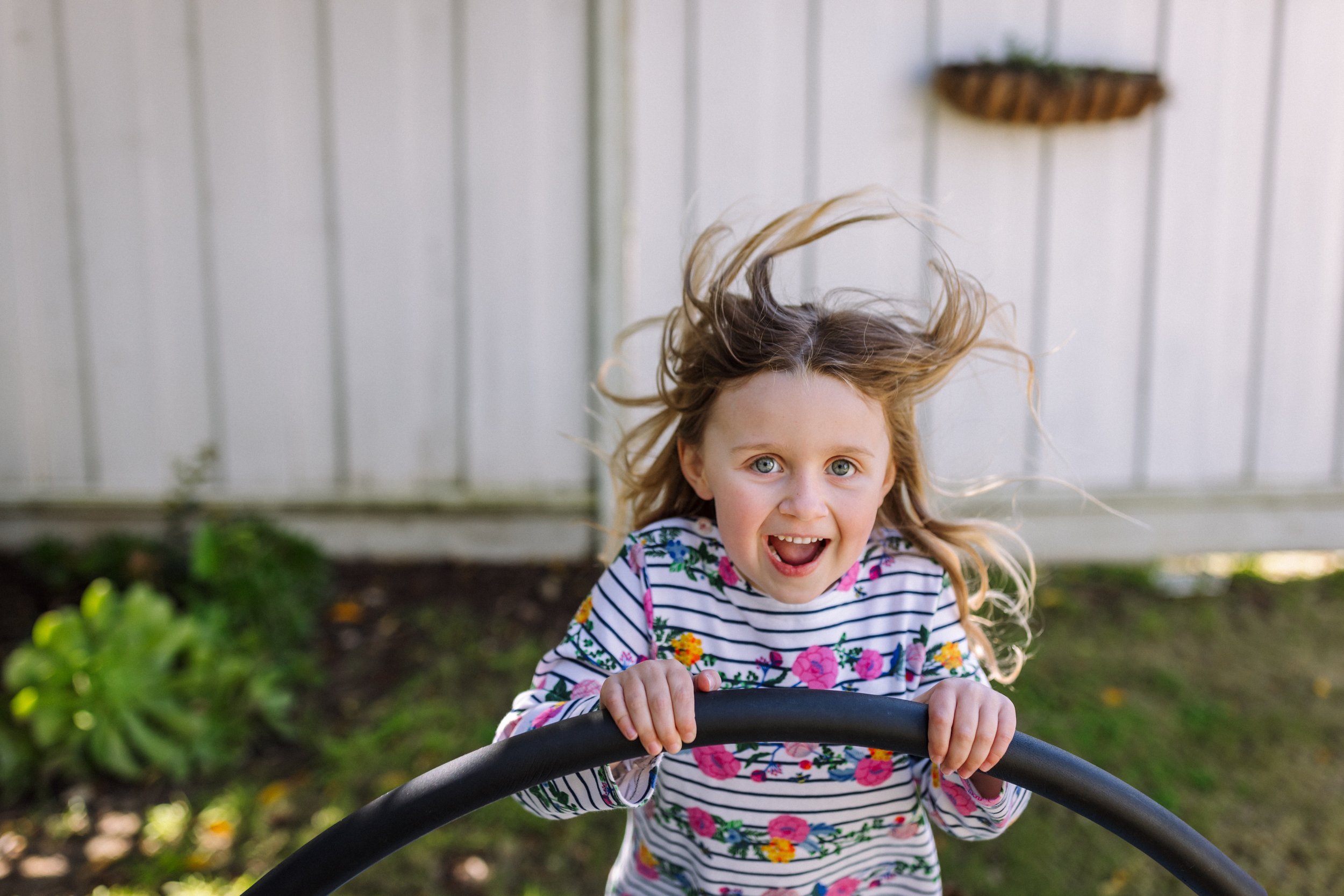 preschool girl laughing and looking at camera while she's jumping on a small trampoline by herself