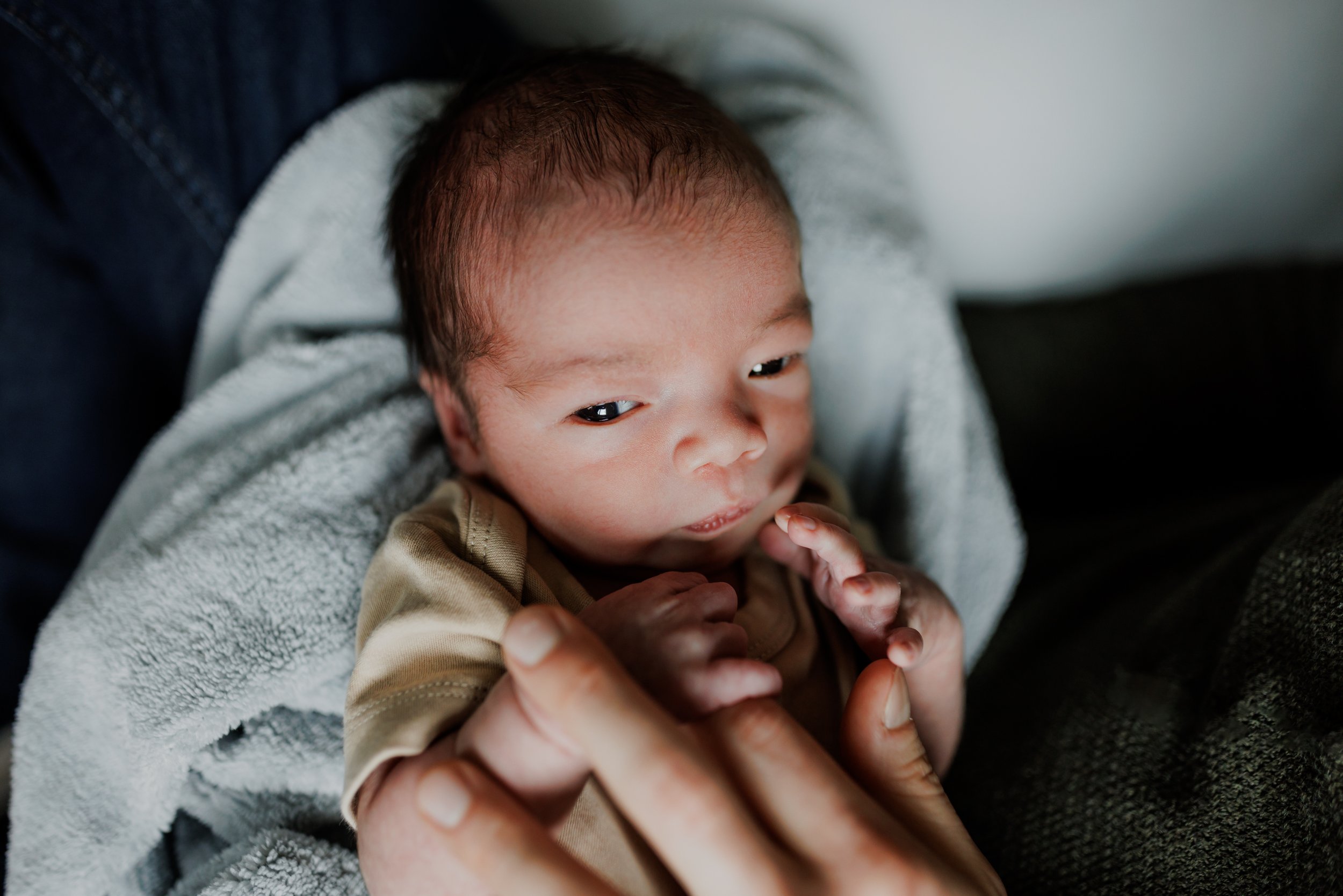 portrait of newborn laying on a blue blanket with his eyes open and touching dad's fingers