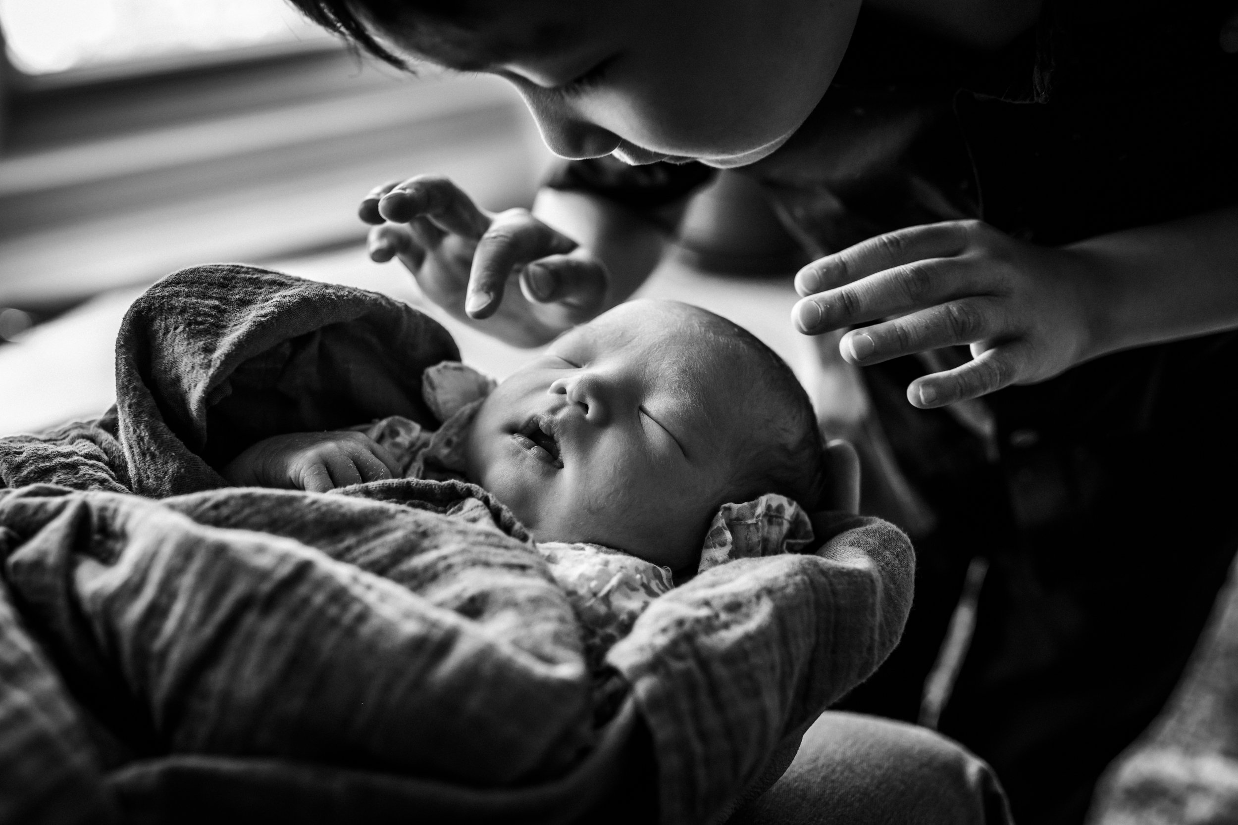 close up of a boy leaning over his newborn sister with his hands up as if he's about to touch her gently