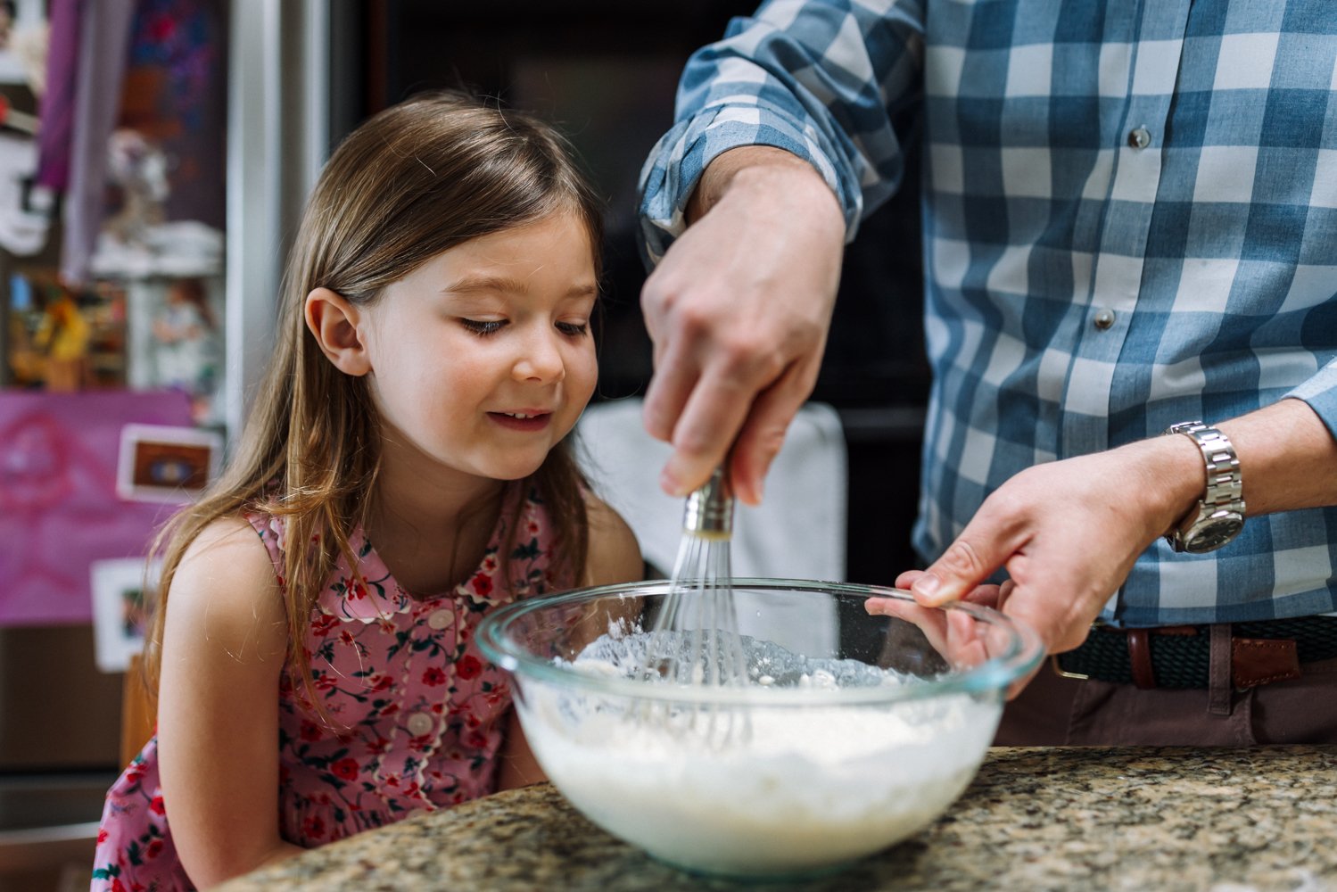 daughter looking on as her dad mixes pancake batter in a large bowl