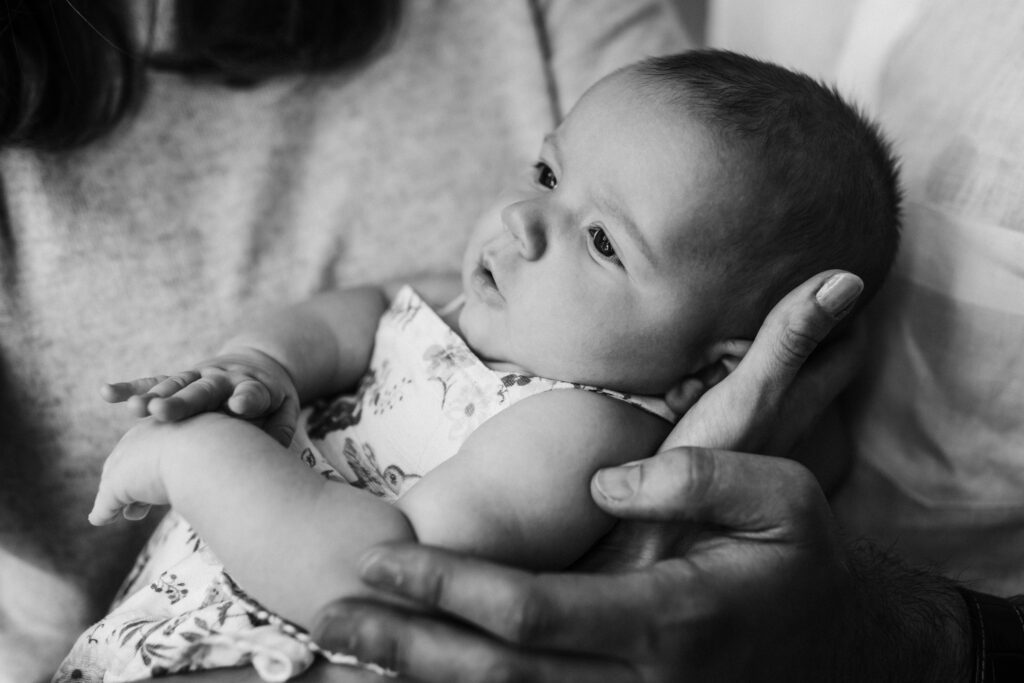 profile of newborn in flowered dress in mom and dad's hands