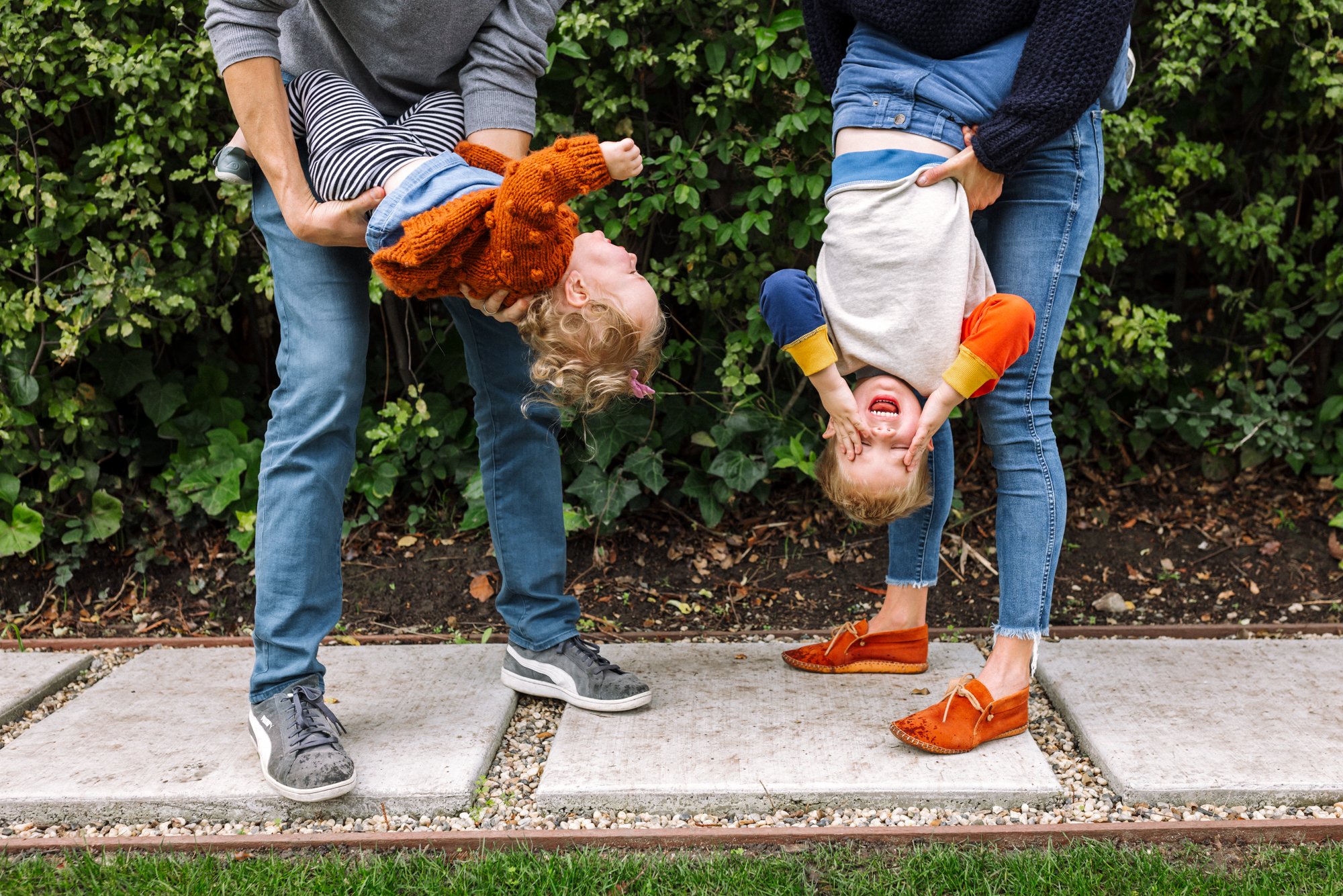 parents standing in a park holding their two children upside down as the kids both laugh