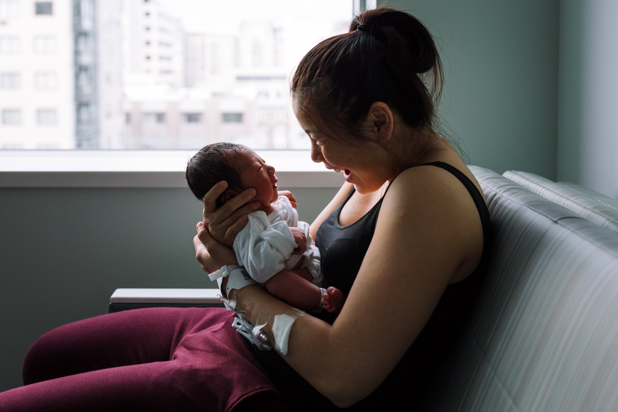 mom holding new baby in the hospital and smiling at him as he gazes at her