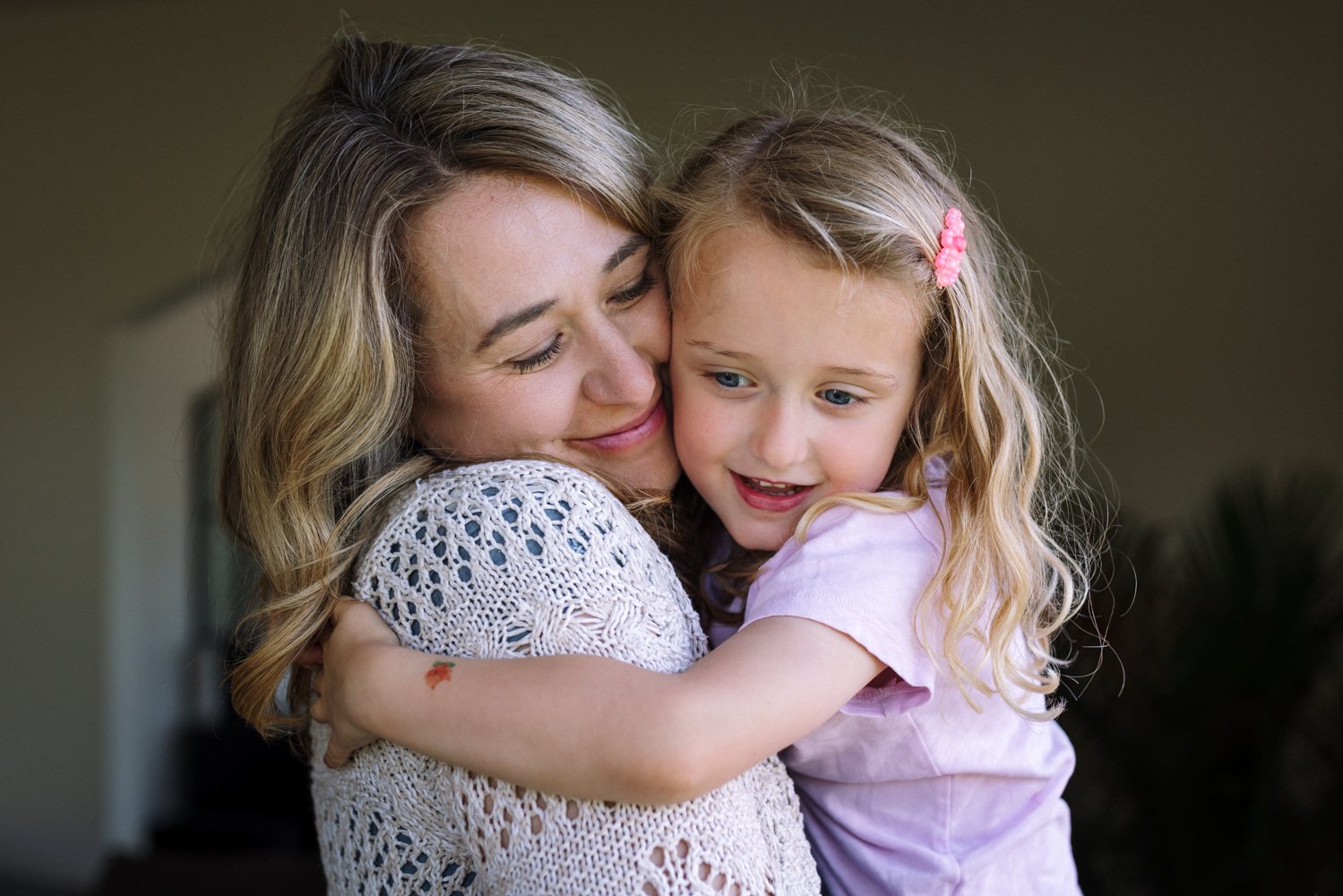 mom holding daughter close and smiling while hugging her