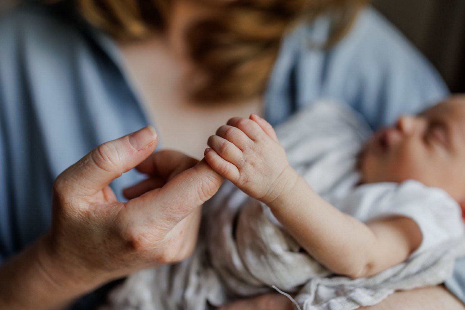 newborn hand wrapped around mom's finger at home