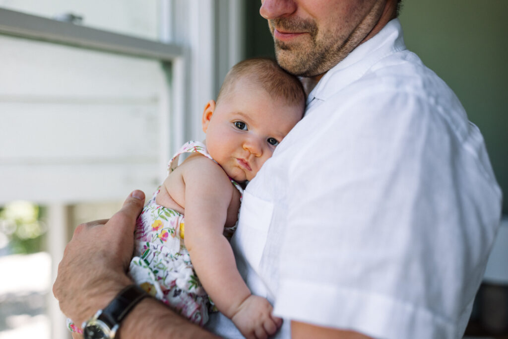 newborn resting head on dad's chest and looking at camera with eyes wide open at home