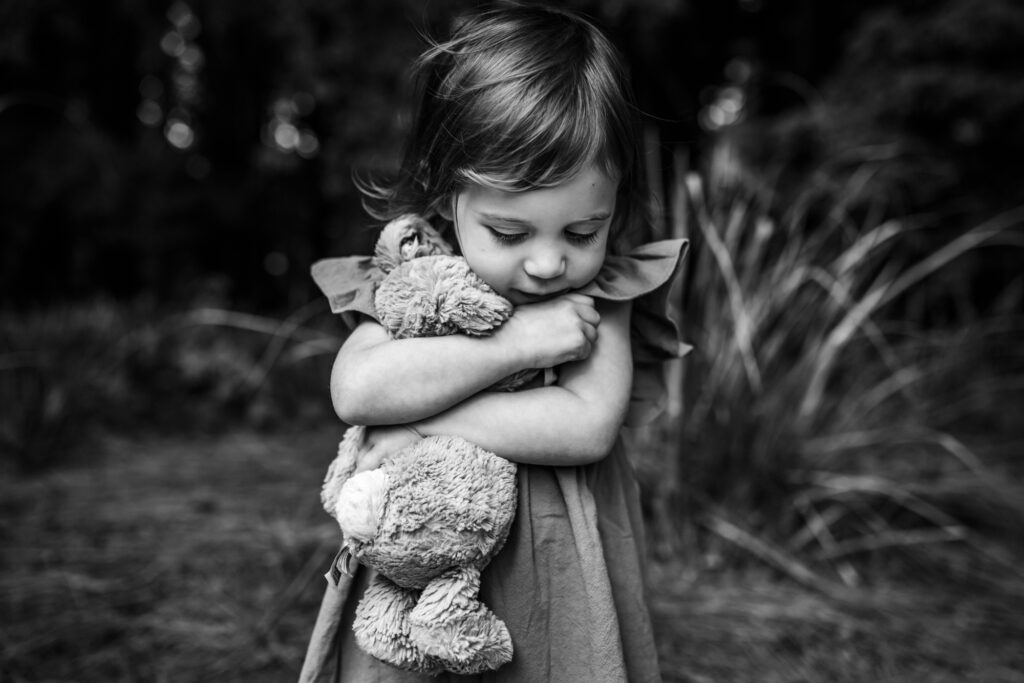 Child hugging a stuffed animal and looking down during outdoor family session