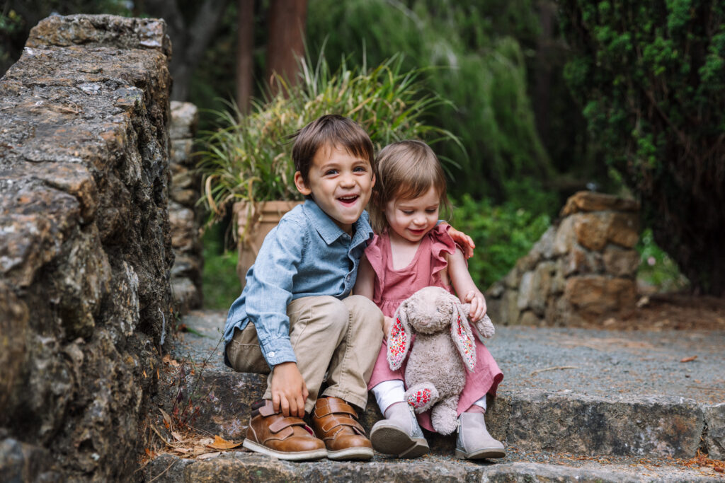 Brother and sister smiling and sitting together on a stone wall