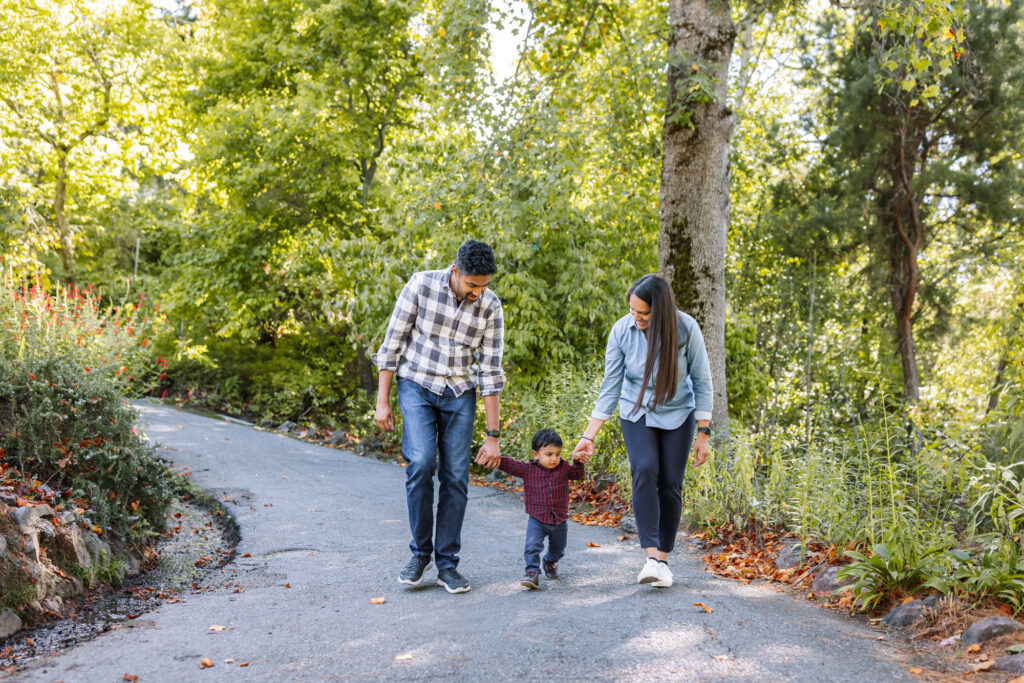 Family walking down a tree-lined path holding their toddler's hands