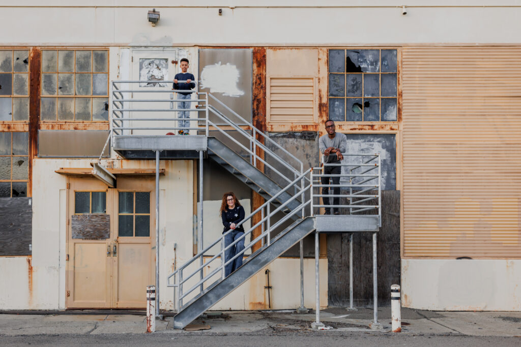Family standing on metal stairs against a rustic industrial building in Alameda