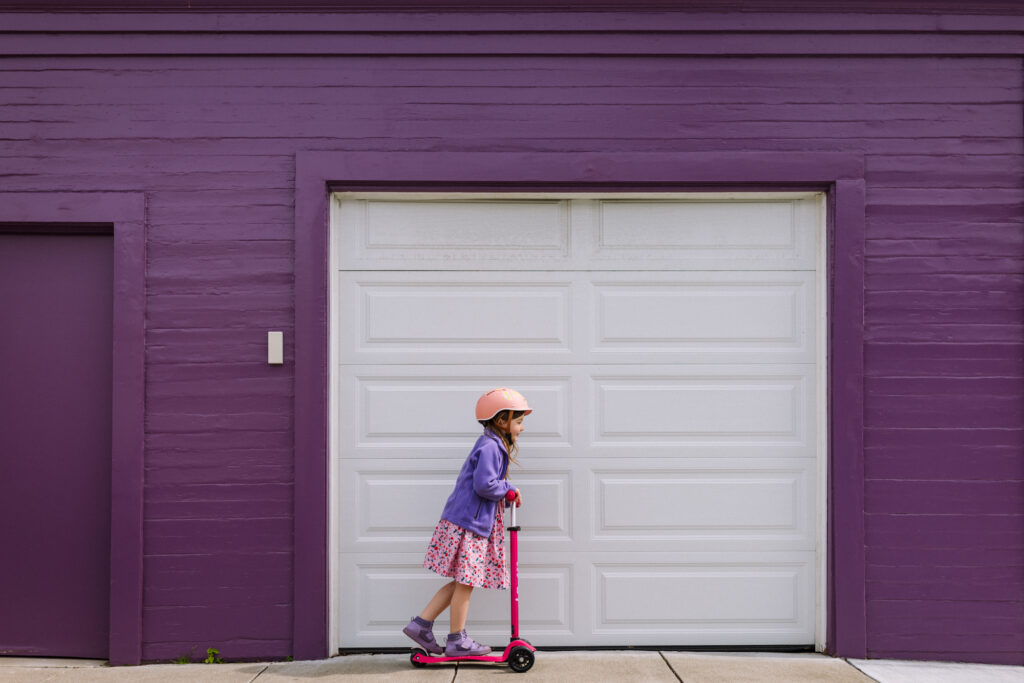 Young girl riding a scooter in front of a purple garage in Bay Area