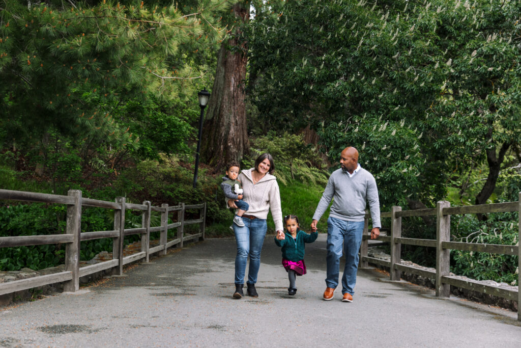 Parents holding hands with two young children on a wooded trail in the East Bay