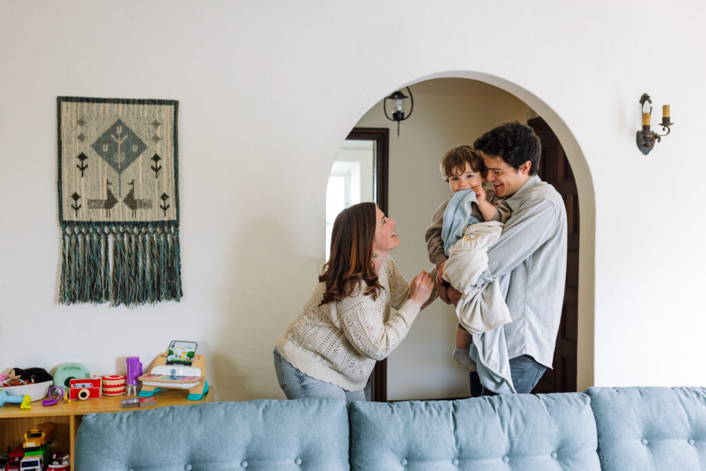 Parents playing with toddler through an arched doorway inside their home