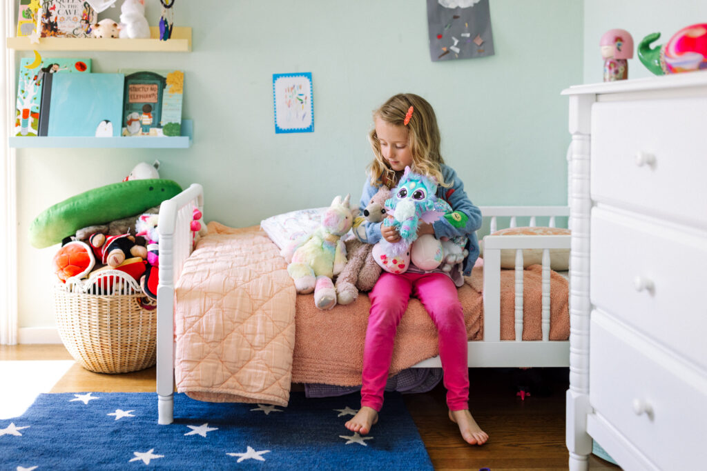 Young girl sitting on her bed with several stuffed animals during an in-home session
