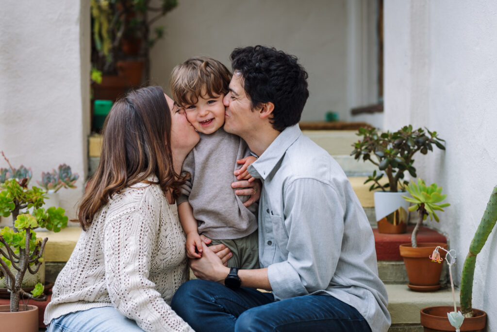 Parents kissing toddler on the porch steps during a lifestyle session