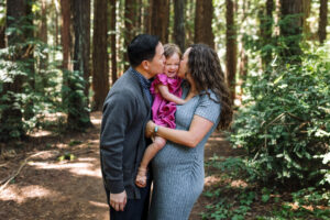 Family snuggling with toddler during maternity session in Oakland woods